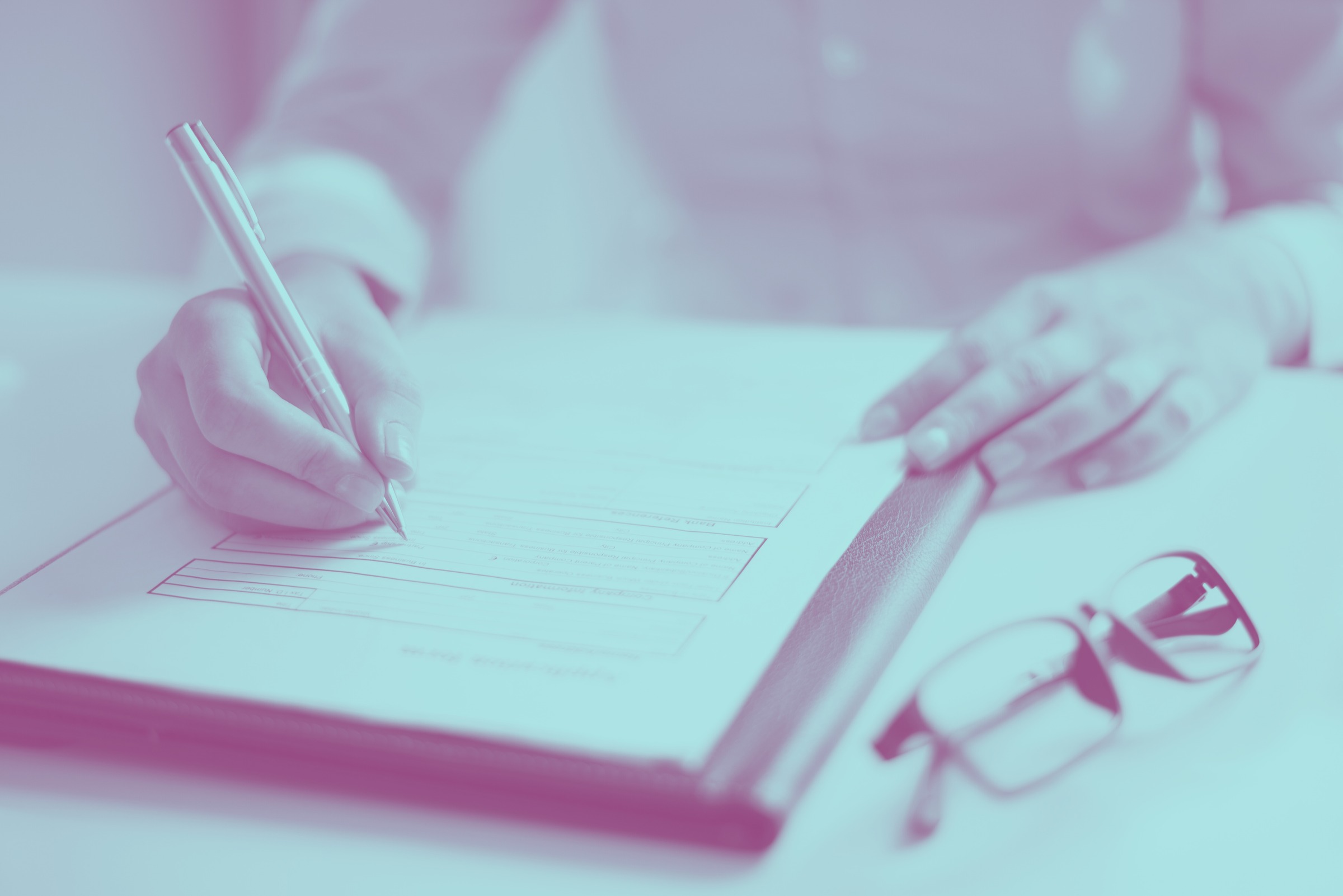 A person completing a form on a clipboard beside a pair of glasses.