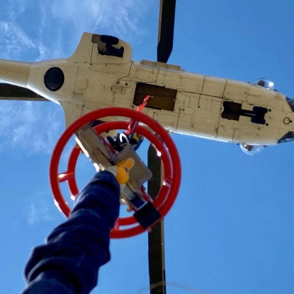 Underside view of ARC helicopter lifting a load near powerline hardware
