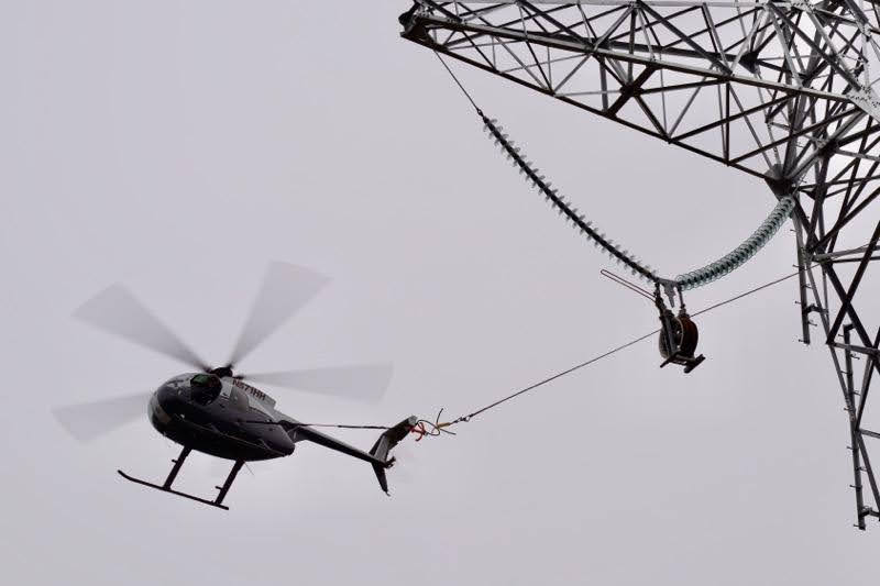Helicopter pulling wire during utility powerline stringing operation
