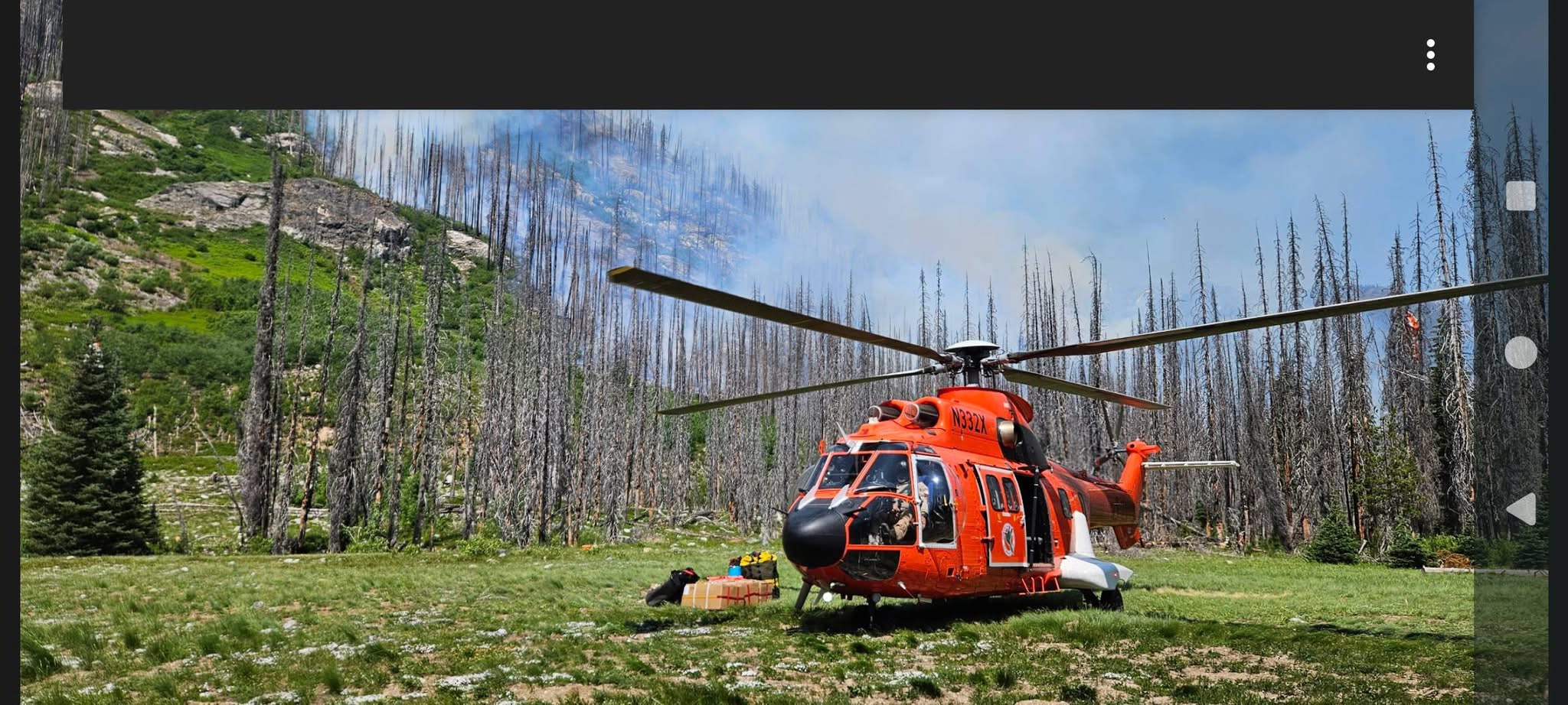 Firefighting helicopter landed near active wildfire with smoke visible in burned forest