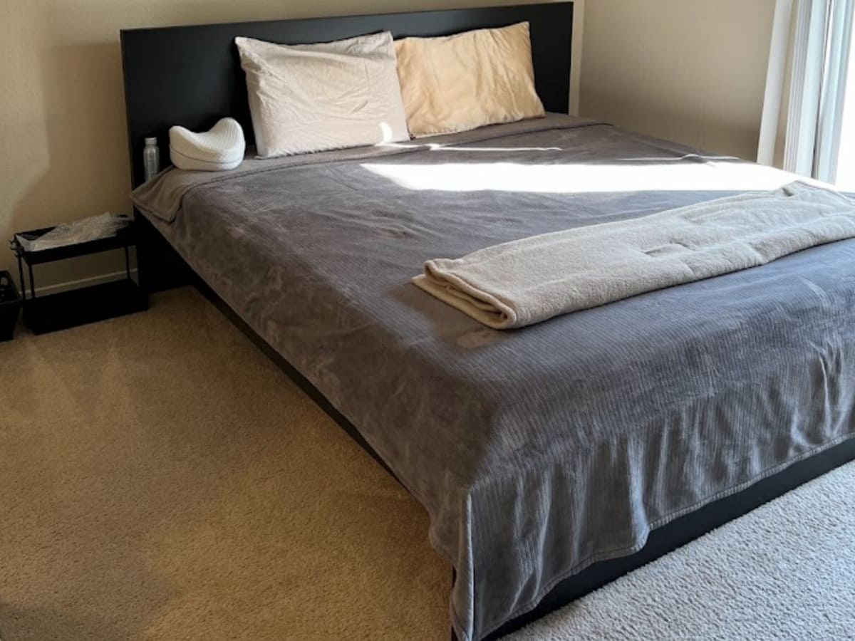 Clean and neatly made bed with gray bedding on a carpeted floor, highlighting thorough bedroom cleaning and carpet care services in Napa