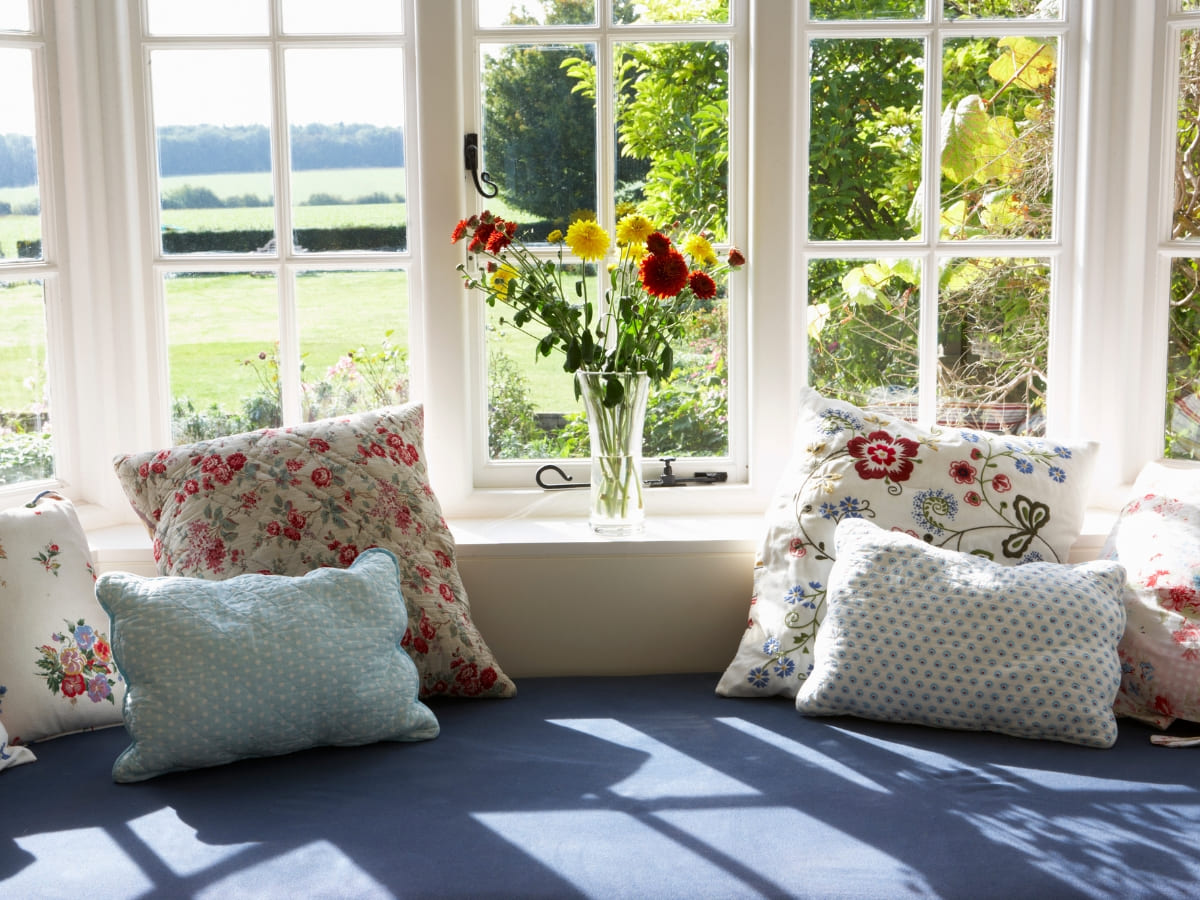 Bright and inviting window seat with floral cushions, overlooking a lush green garden, perfect for relaxation.