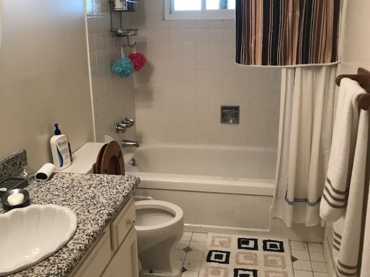 Clean and simple bathroom with a classic white bathtub, granite countertop, and striped shower curtain, all neatly organized.