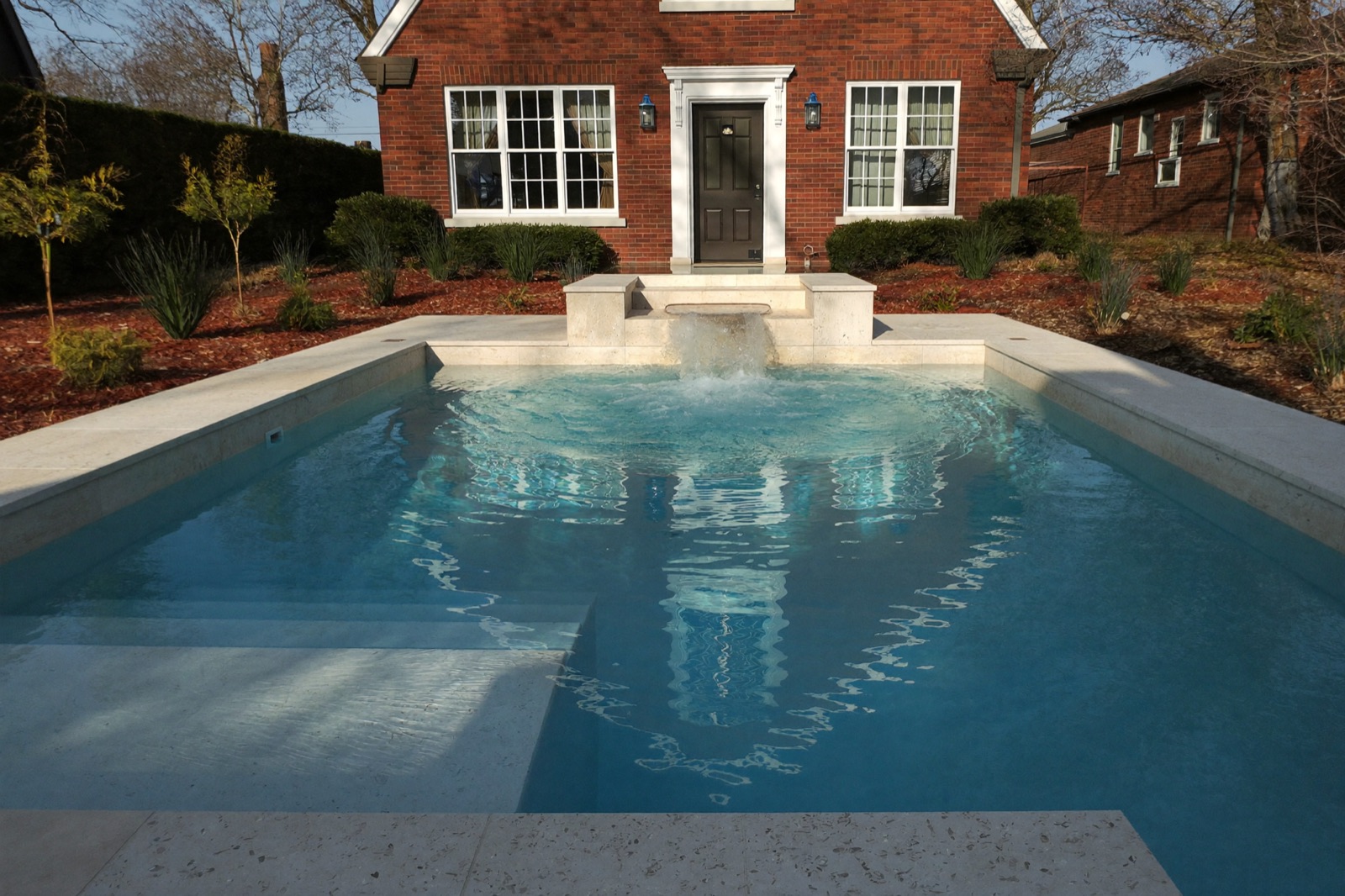 Custom gunite pool with an integrated raised spa spilling into the water and a travertine pool deck