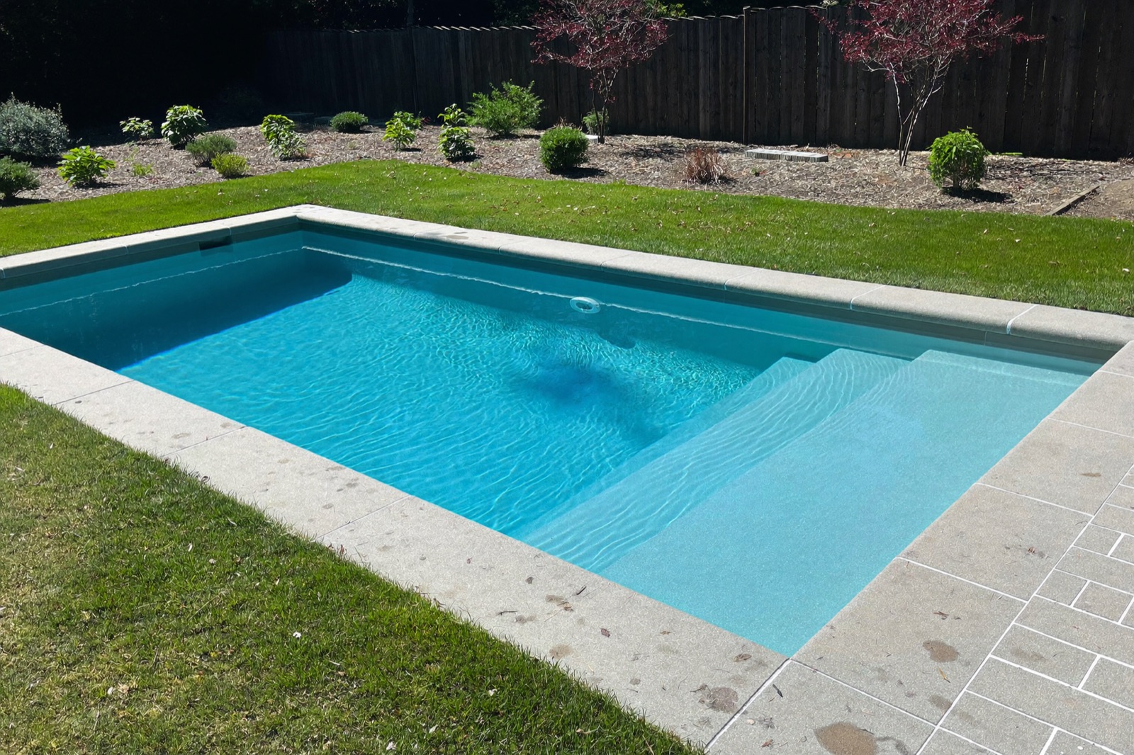 Rectangular fiberglass pool with a tanning ledge and a paver pool deck