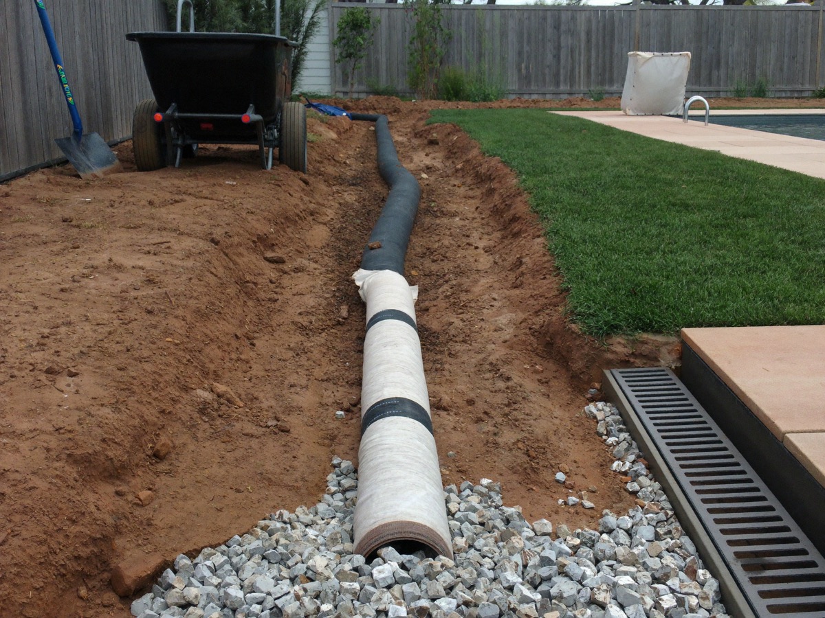 French drain pipe in gravel and a channel drain at the edge of a pool deck