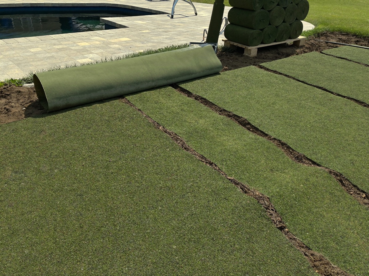 Fresh sod rolls being laid over graded soil