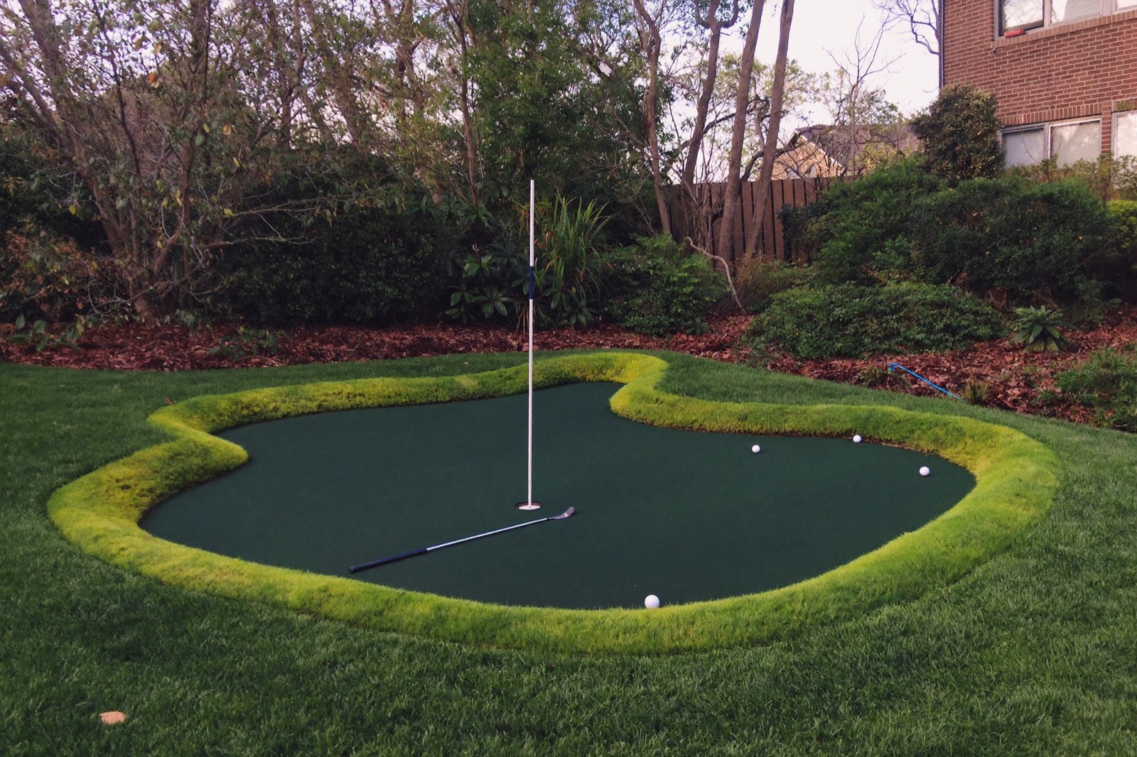Backyard synthetic putting green with two cups, flagsticks and a fringe collar