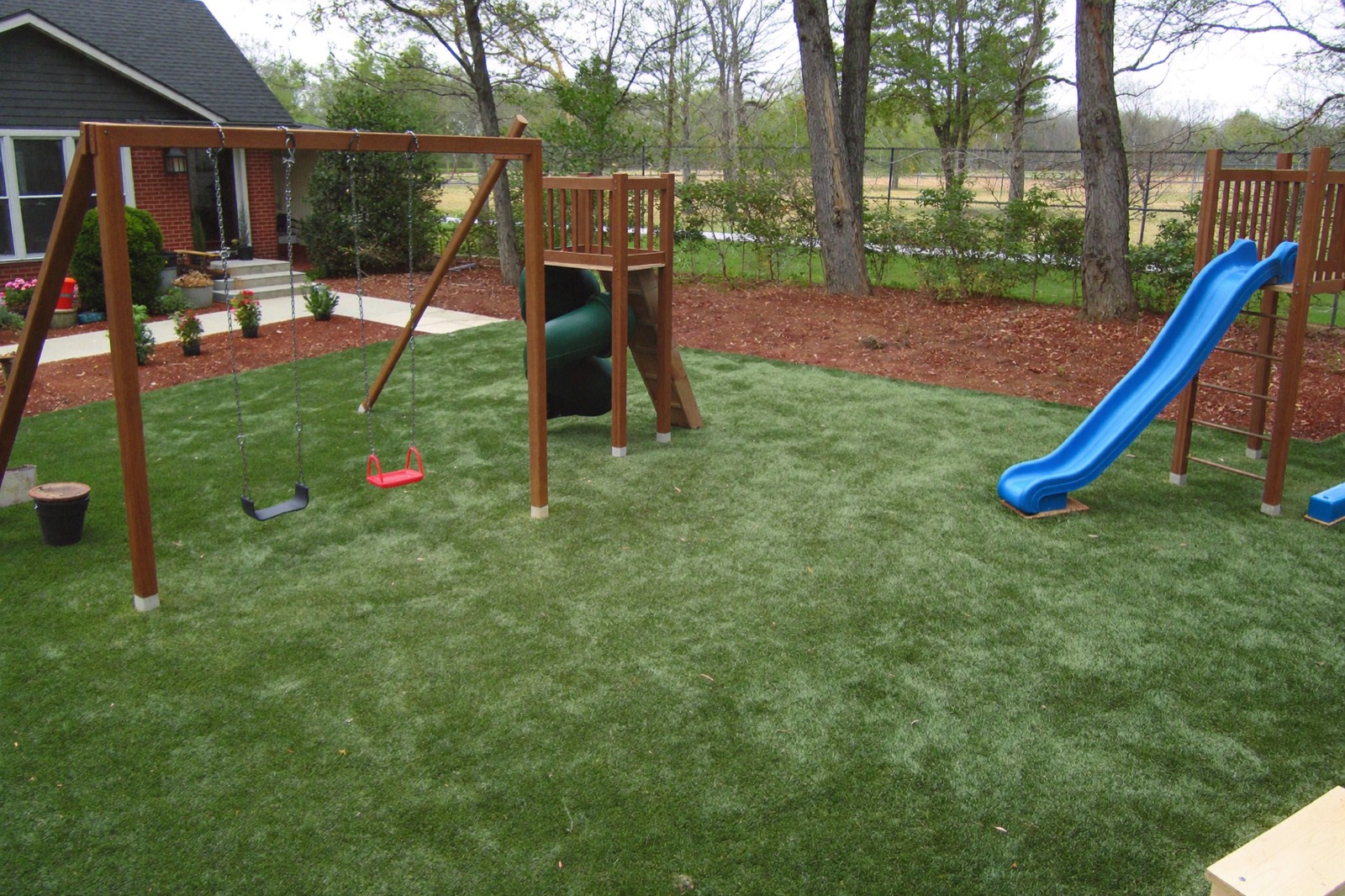 Backyard swing set and slide over soft artificial playground turf with a padded underlayment