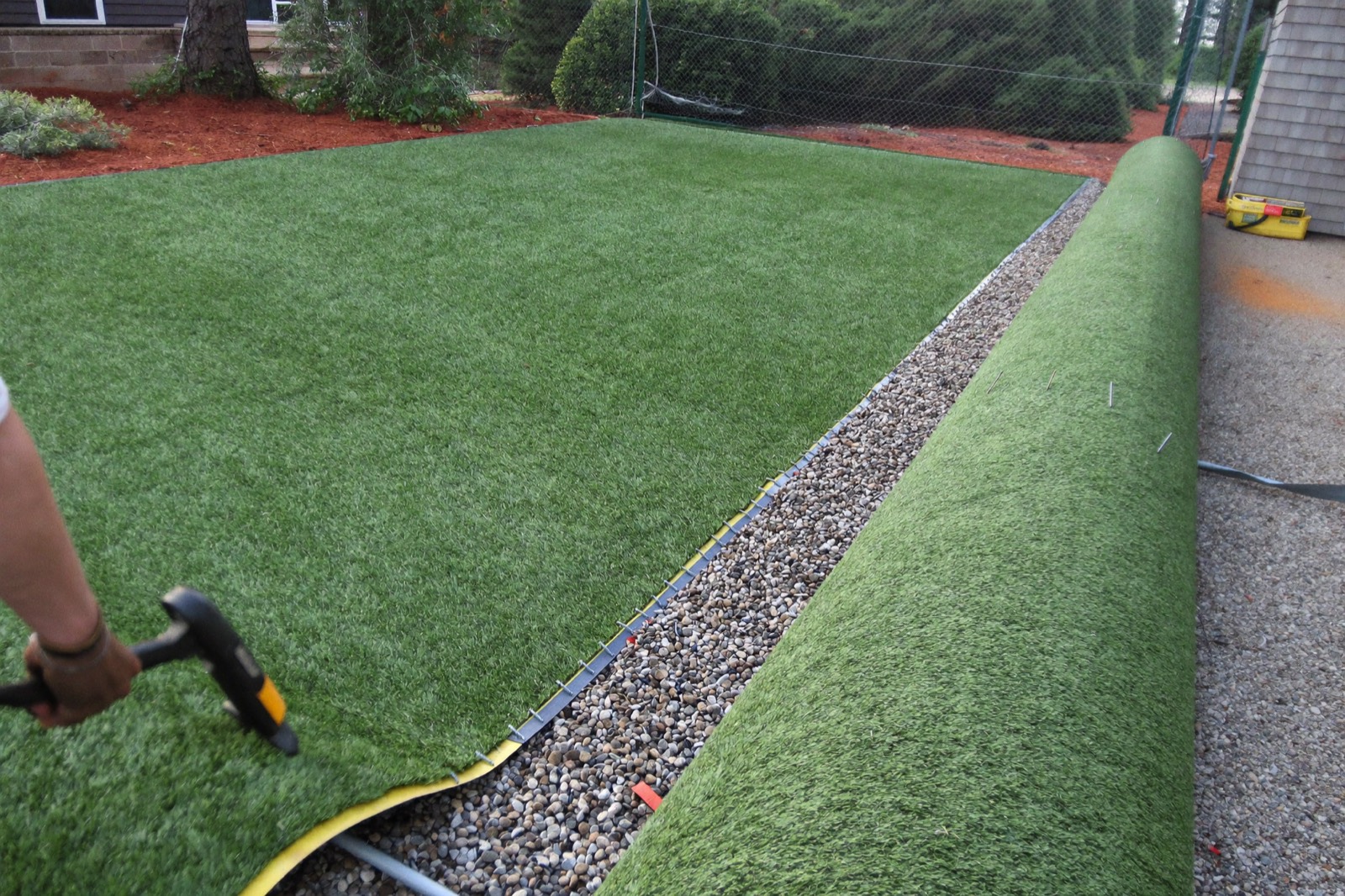 Turf being edge-nailed along a gravel border with the next roll waiting