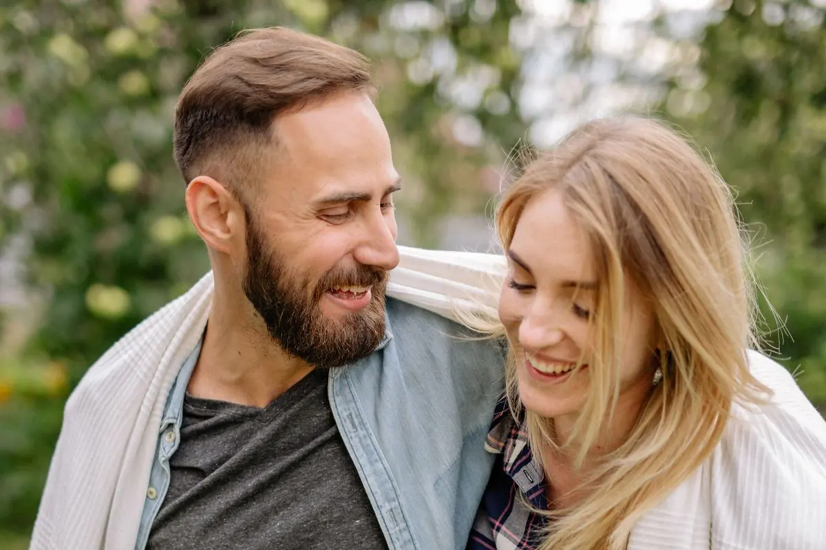 Two people outdoors wrapped in a blanket, both smiling.