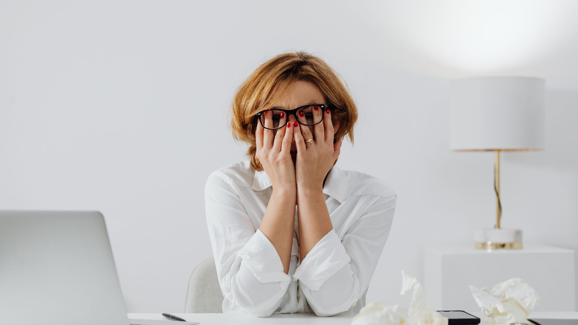 woman with glasses covering her eyes sits at a desk, appearing contemplative and focused on her work 