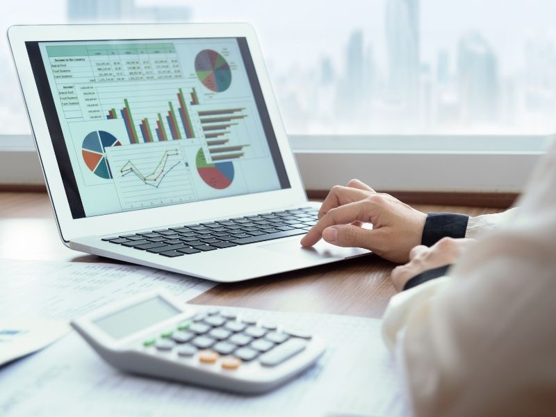 Businesswoman working on a laptop, examining financial data with various charts and statistics visible on the scree
