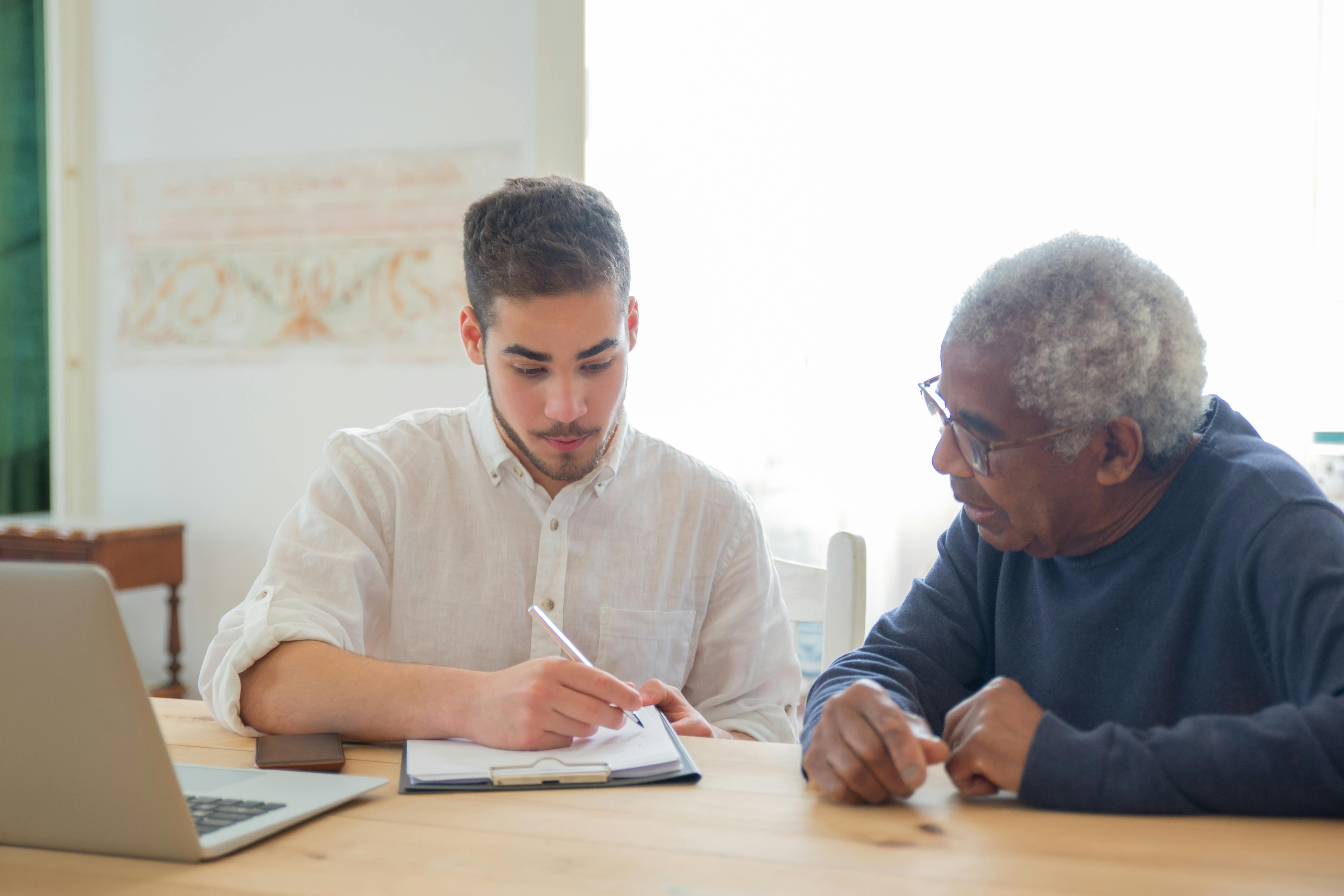 Adult son reviewing long-term care paperwork at home with his elderly father