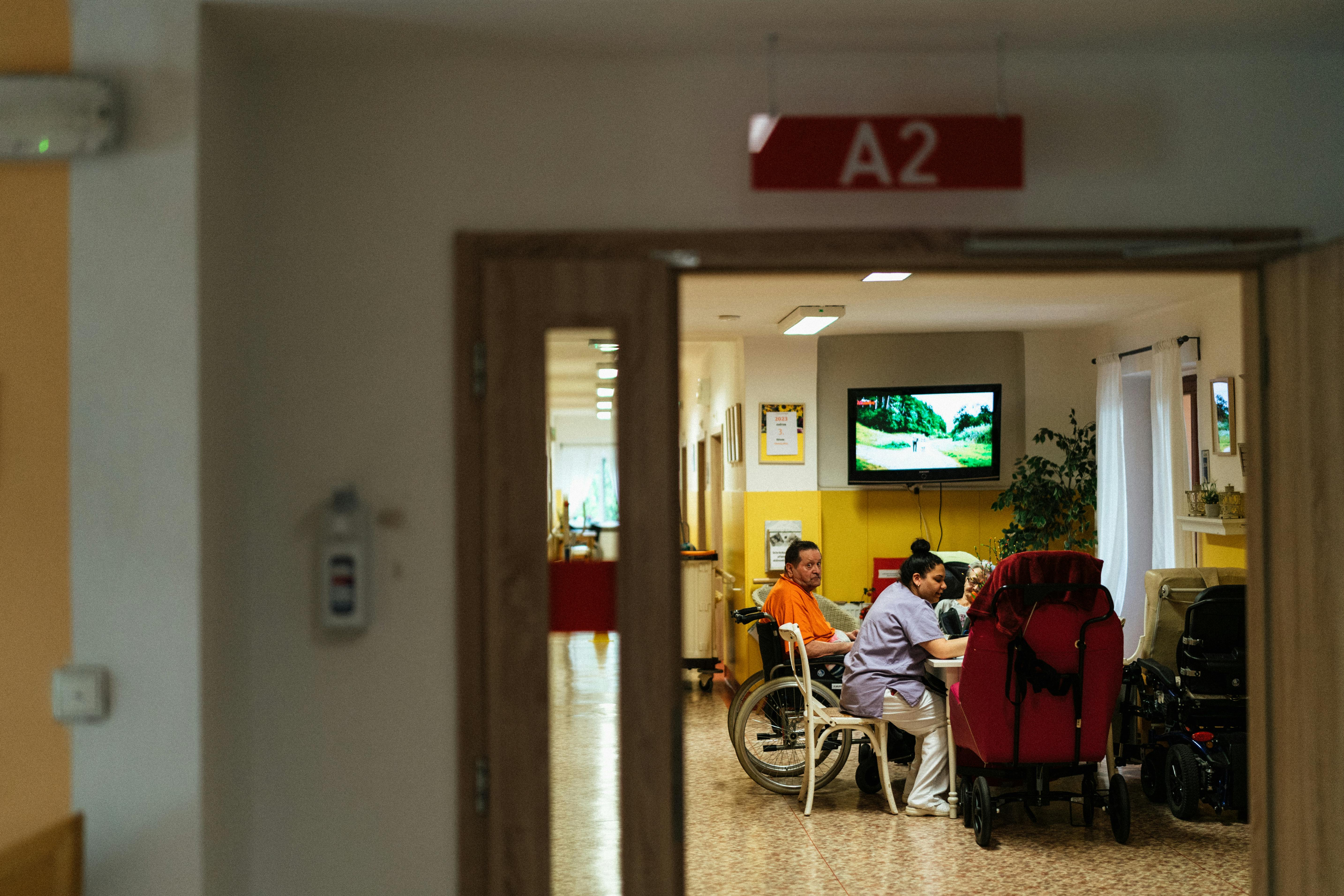Nursing home staff assisting resident in wheelchair in communal care facility room