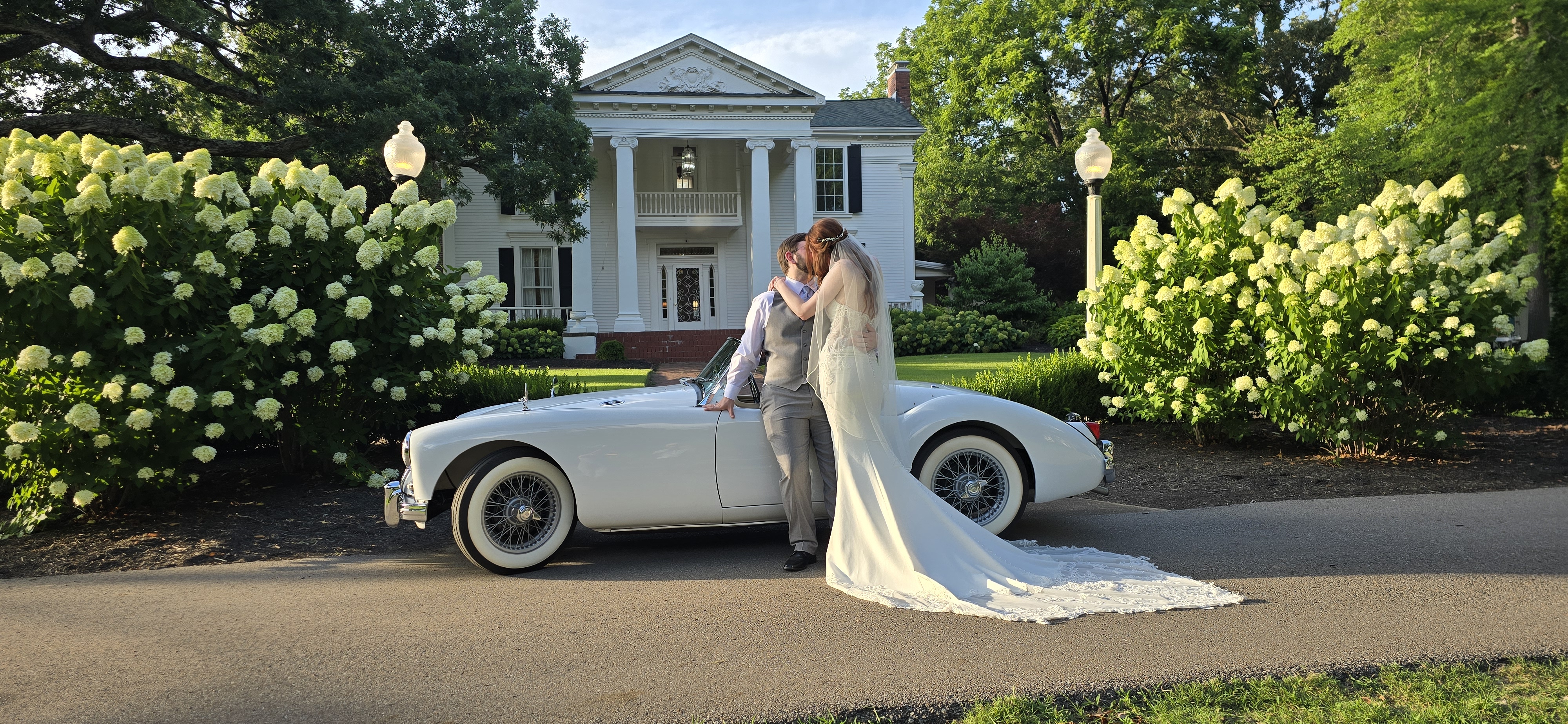 Bride and groom kissing beside the roadster with her veil trailing