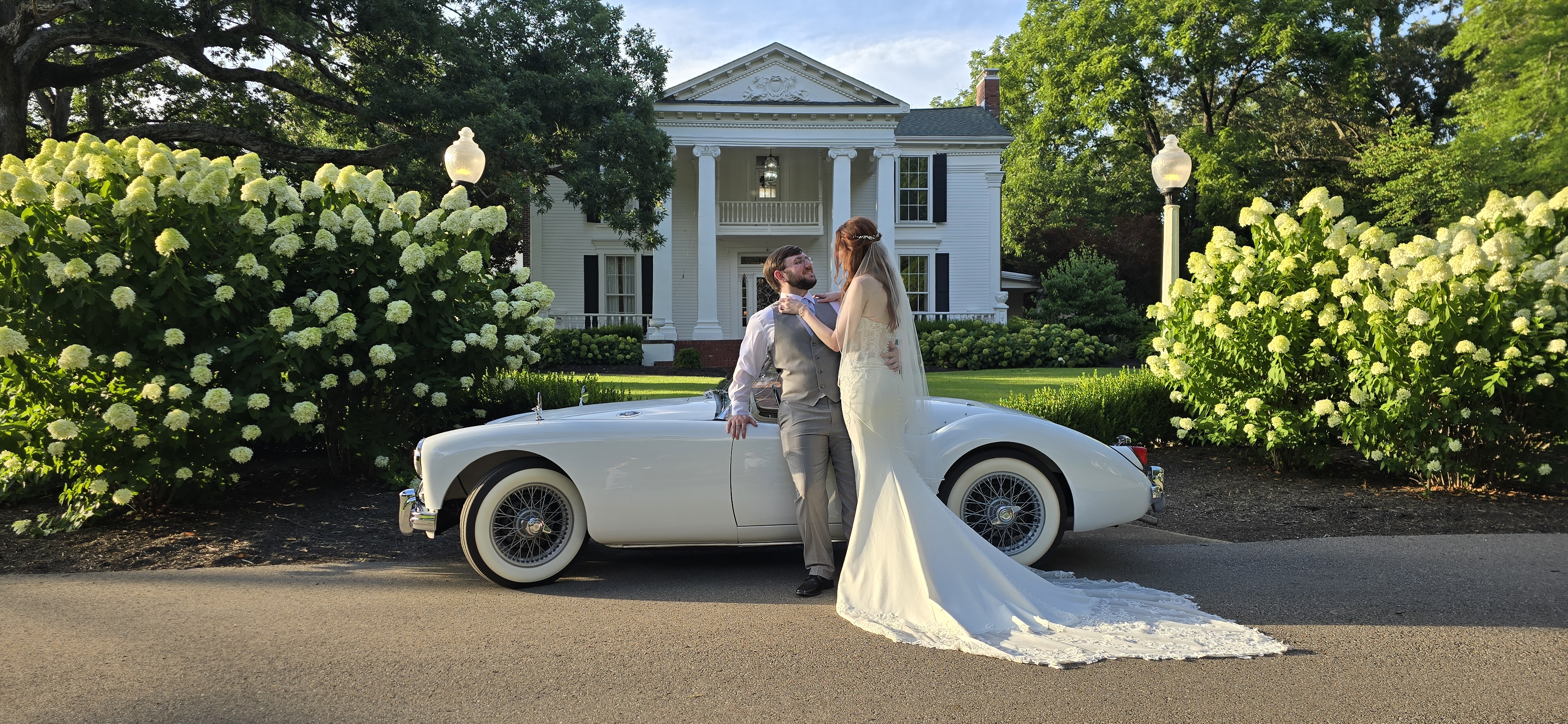 Bride and groom embracing beside the roadster at a columned mansion