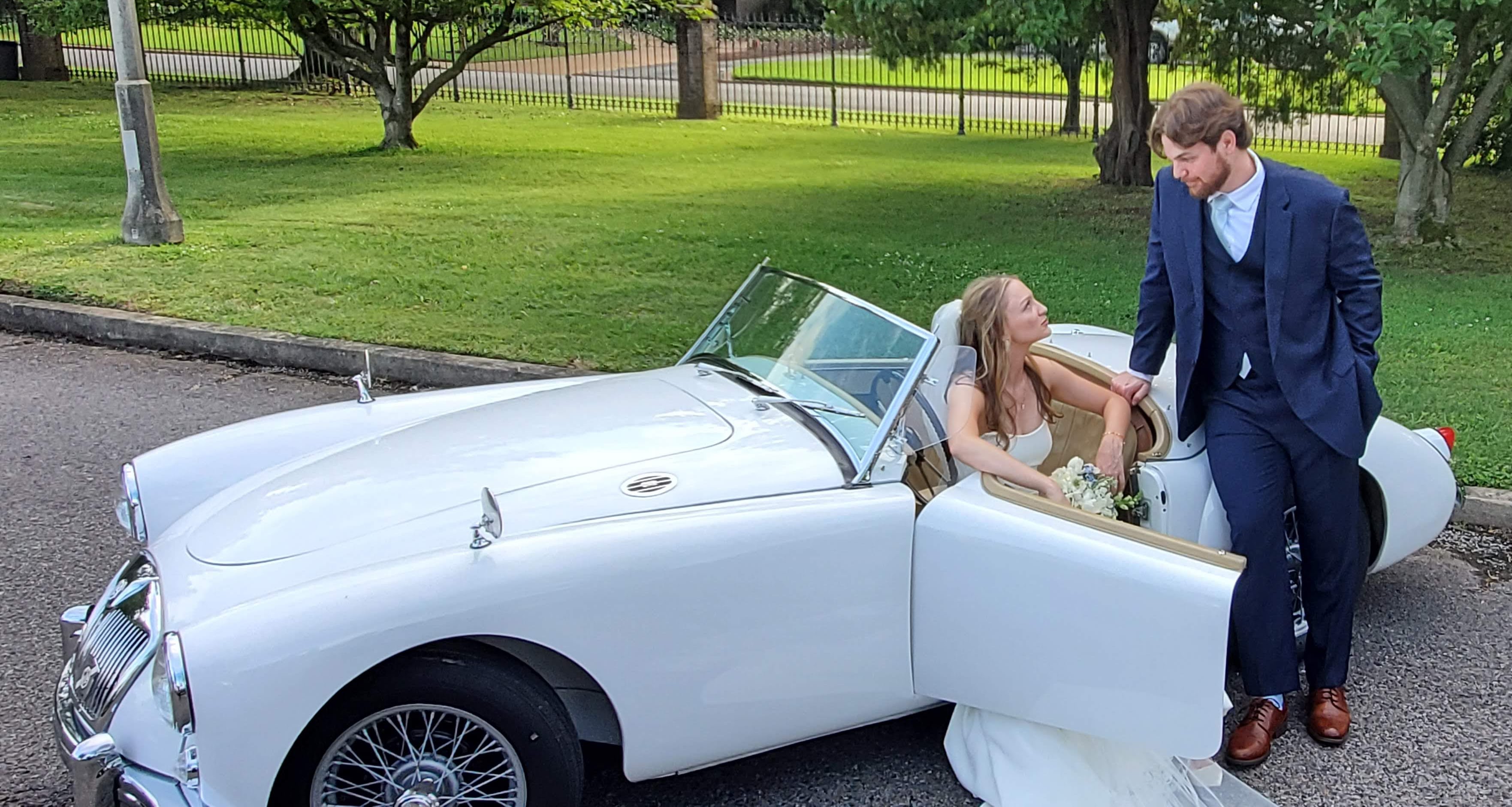 Bride seated in the roadster as the groom leans in