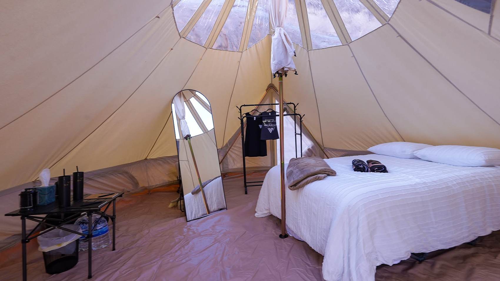 Inside a stargazing yurt: queen bed, full length mirror, clothing rack, clear dome ceiling