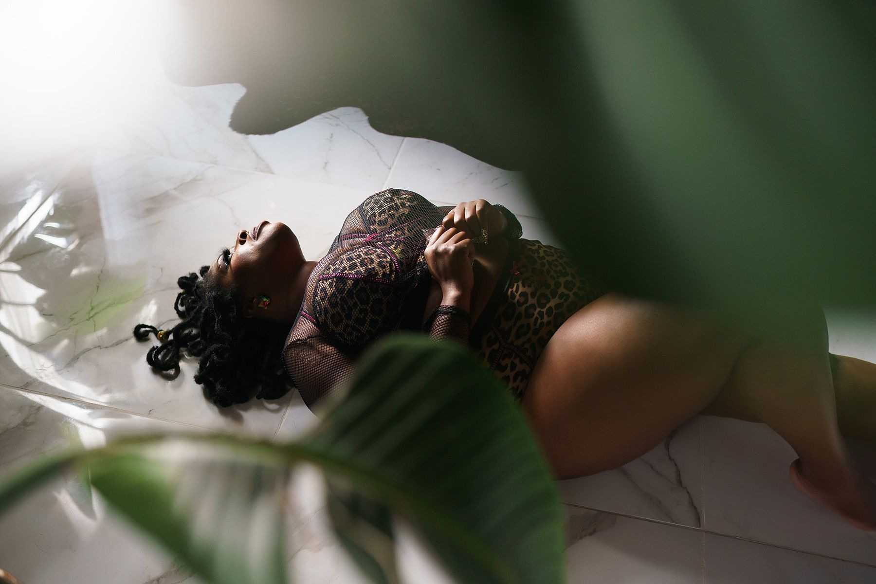 Black woman in leopard lingerie lying on marble framed by leaves, Hampton Roads plus size boudoir