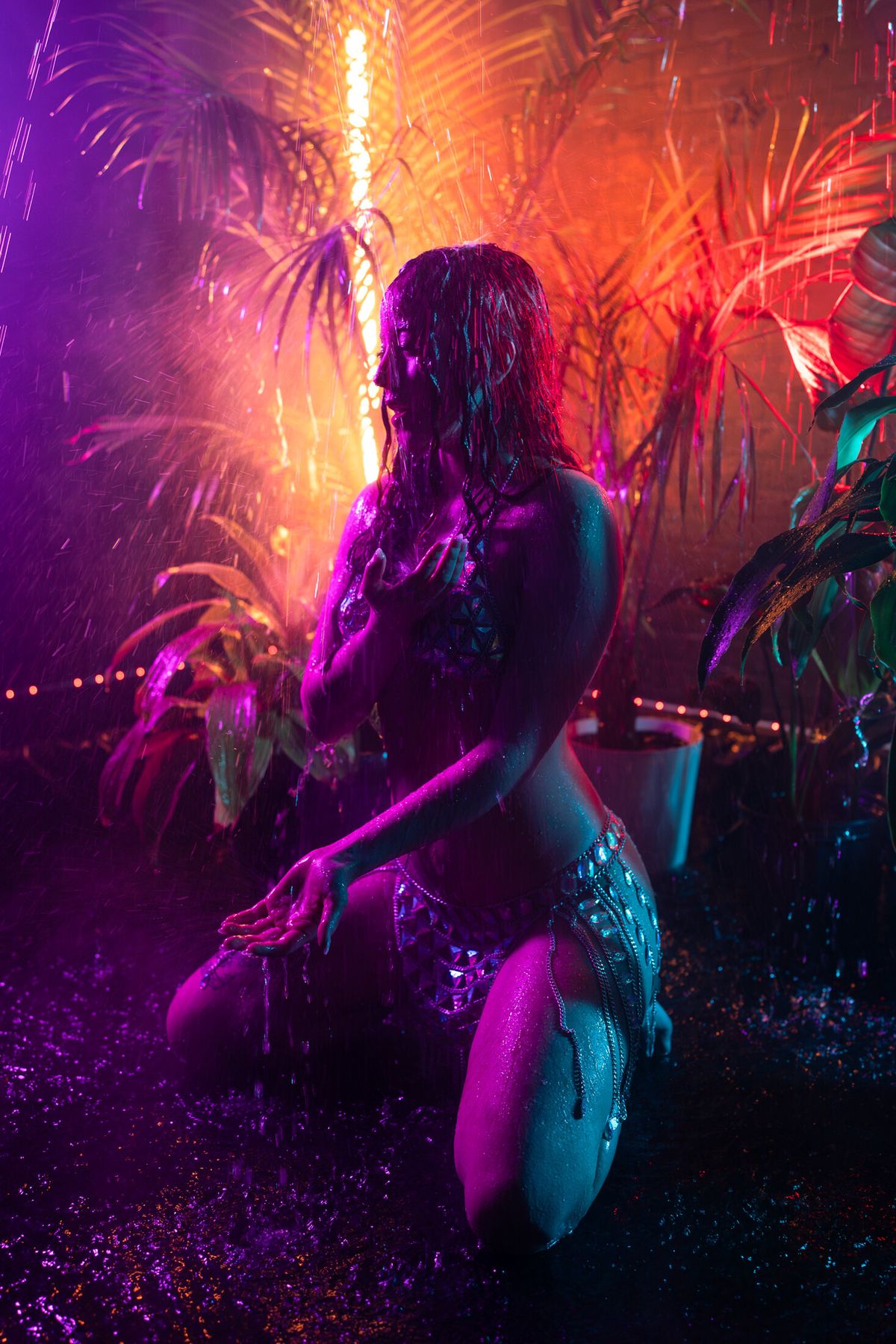 Woman kneeling in the rain under neon light in the rain room at LeZandra Photography, Norfolk, Virginia