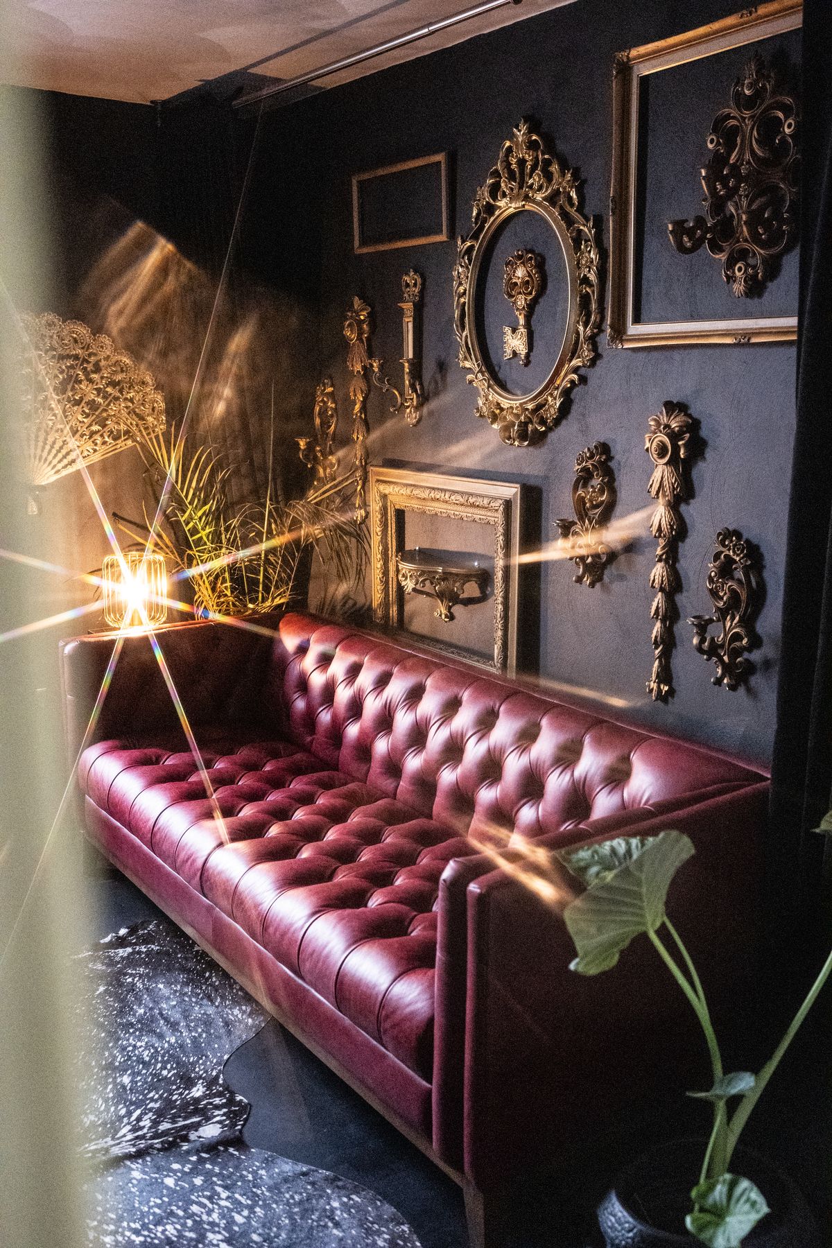Oxblood tufted leather sofa beneath gilded frames at LeZandra Photography’s Hampton Roads boudoir studio