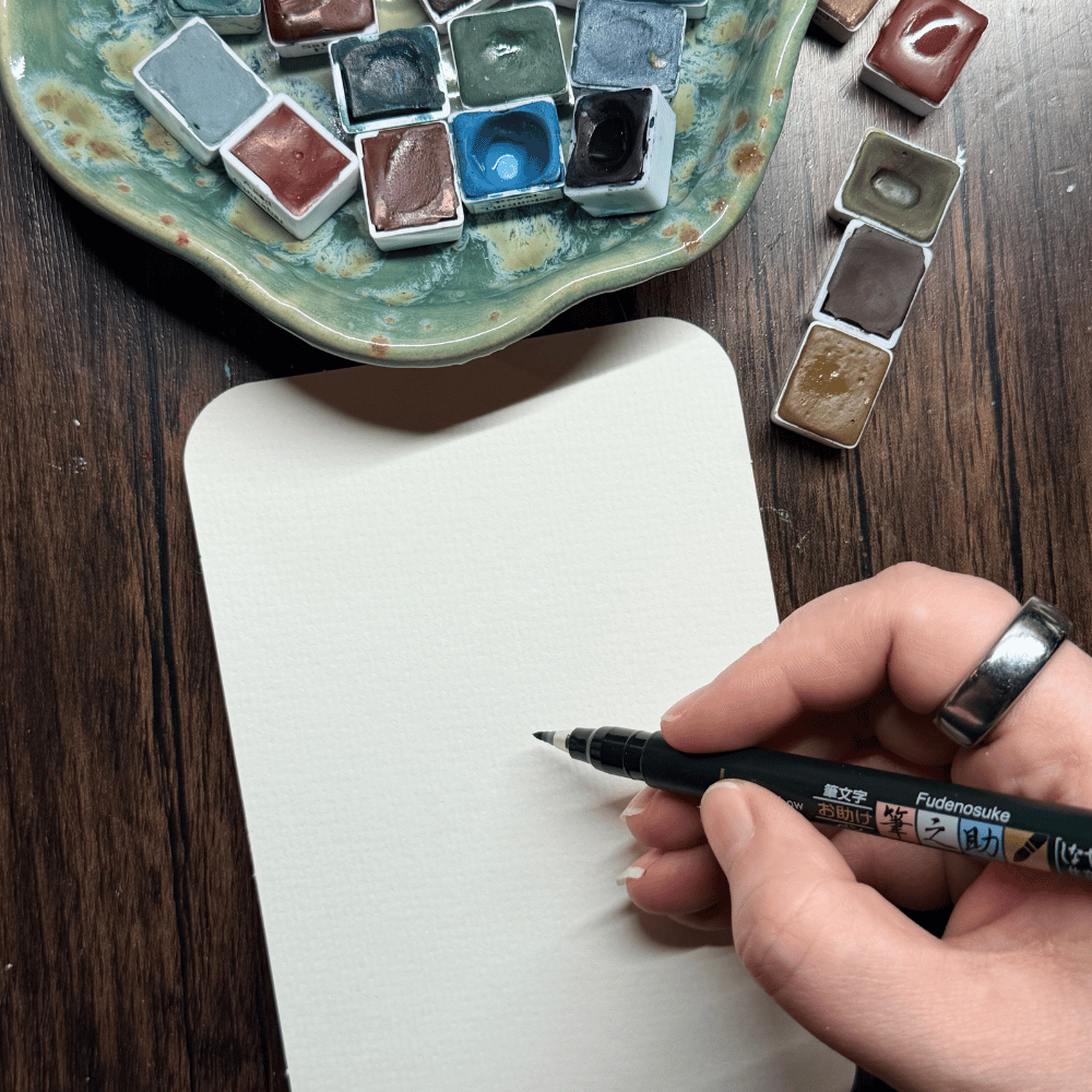 Blank paper with hand, pen and watercolors ready to paint