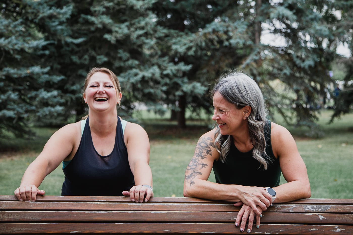 Lindsey Kaupp and Amber Ell laughing together as they lean on a park bench