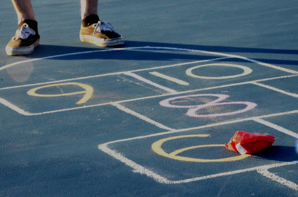 A bean bag lands on a chalk hopscotch grid. In the Challenge competition, players must clear every box marked with a bag.