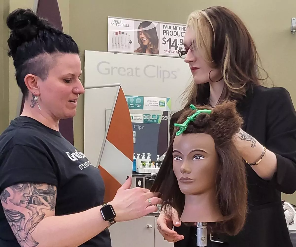 Cosmetology teacher demonstrating haircut techniques on a head model to a Maine student at Great Hair in Maine, supporting student training and skill development.