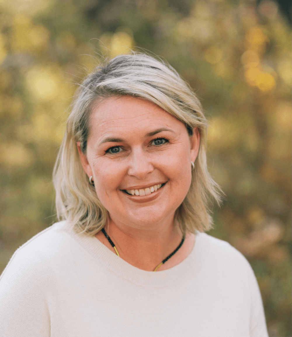 Hannah Renyi, Great Hair in Maine co-owner, smiling in white top with autumn background