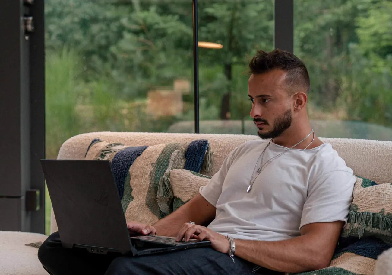 Bruno Souza working on a laptop, sitting on a couch in a glass house