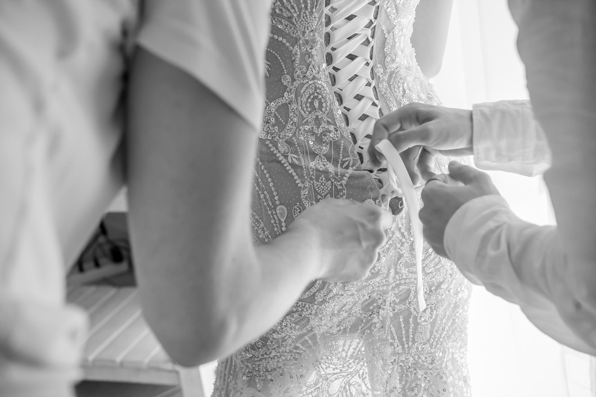 Two pairs of hands lacing up the back of a bride's beaded dress