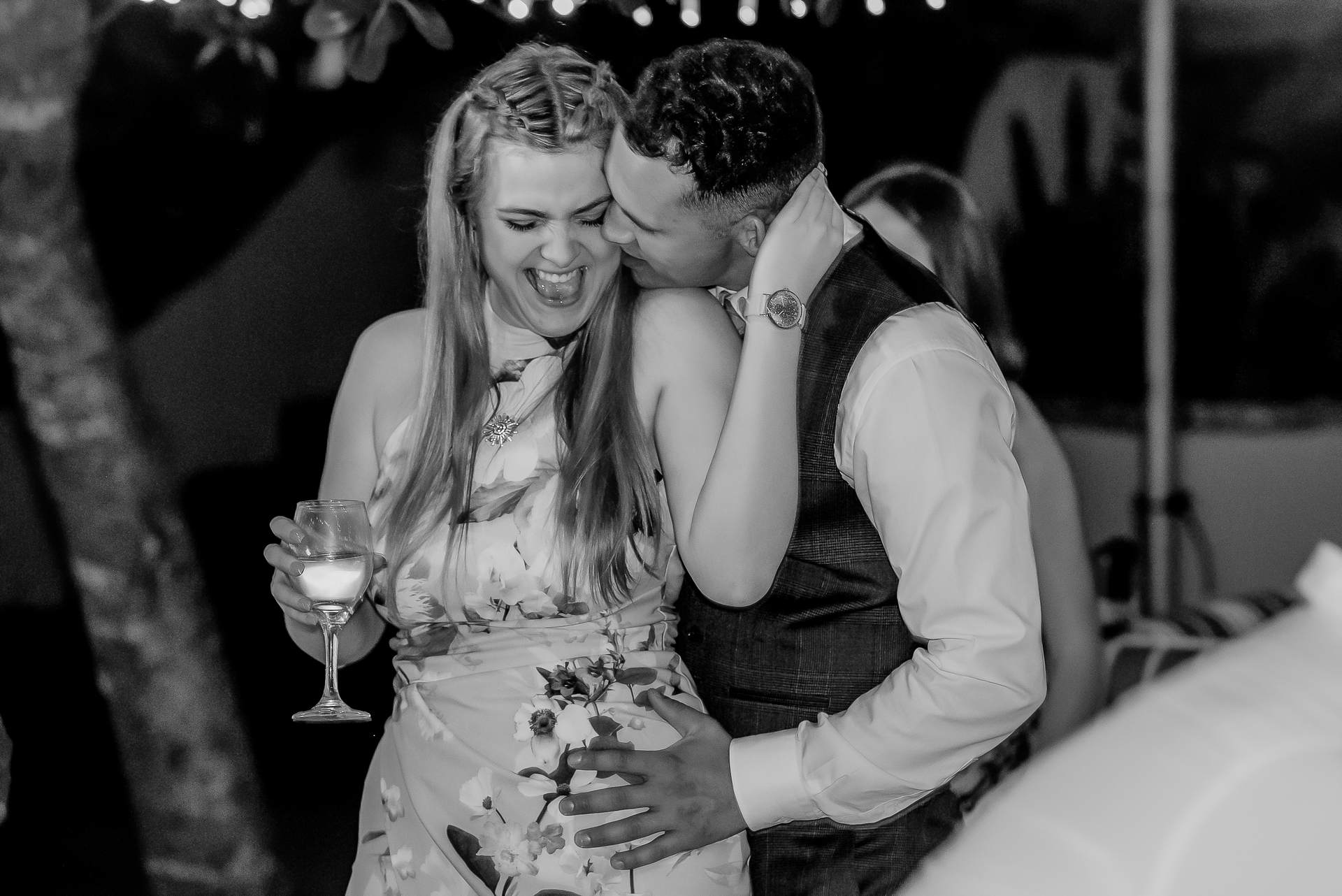 A man kissing a laughing guest on the cheek at a wedding reception