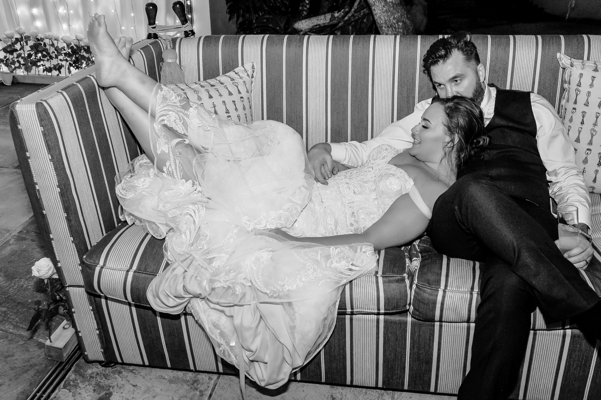 A bride and groom lying back on a striped sofa at their reception