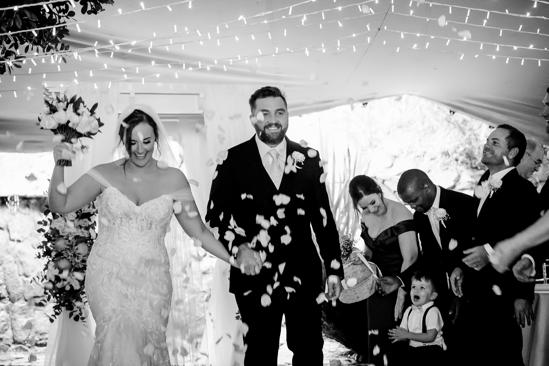 A bride and groom walking out as guests throw petals