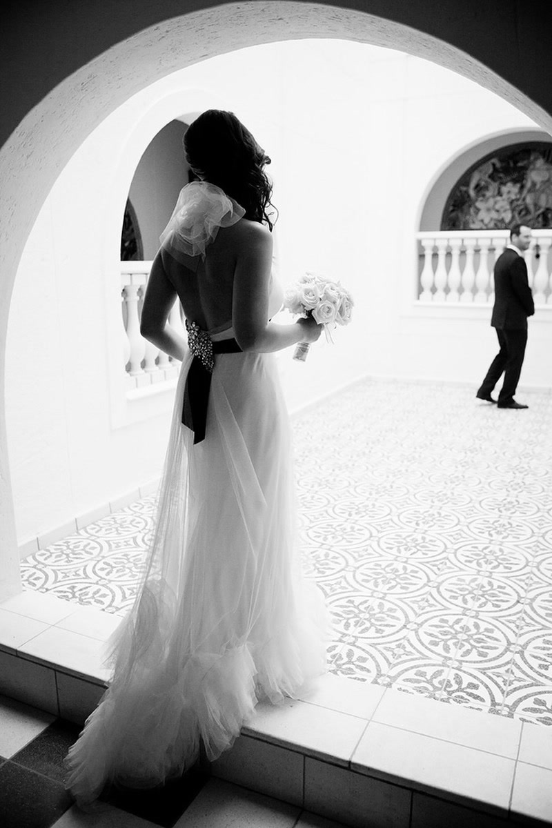 A bride in an archway looking out at her groom, who waits with his back to her