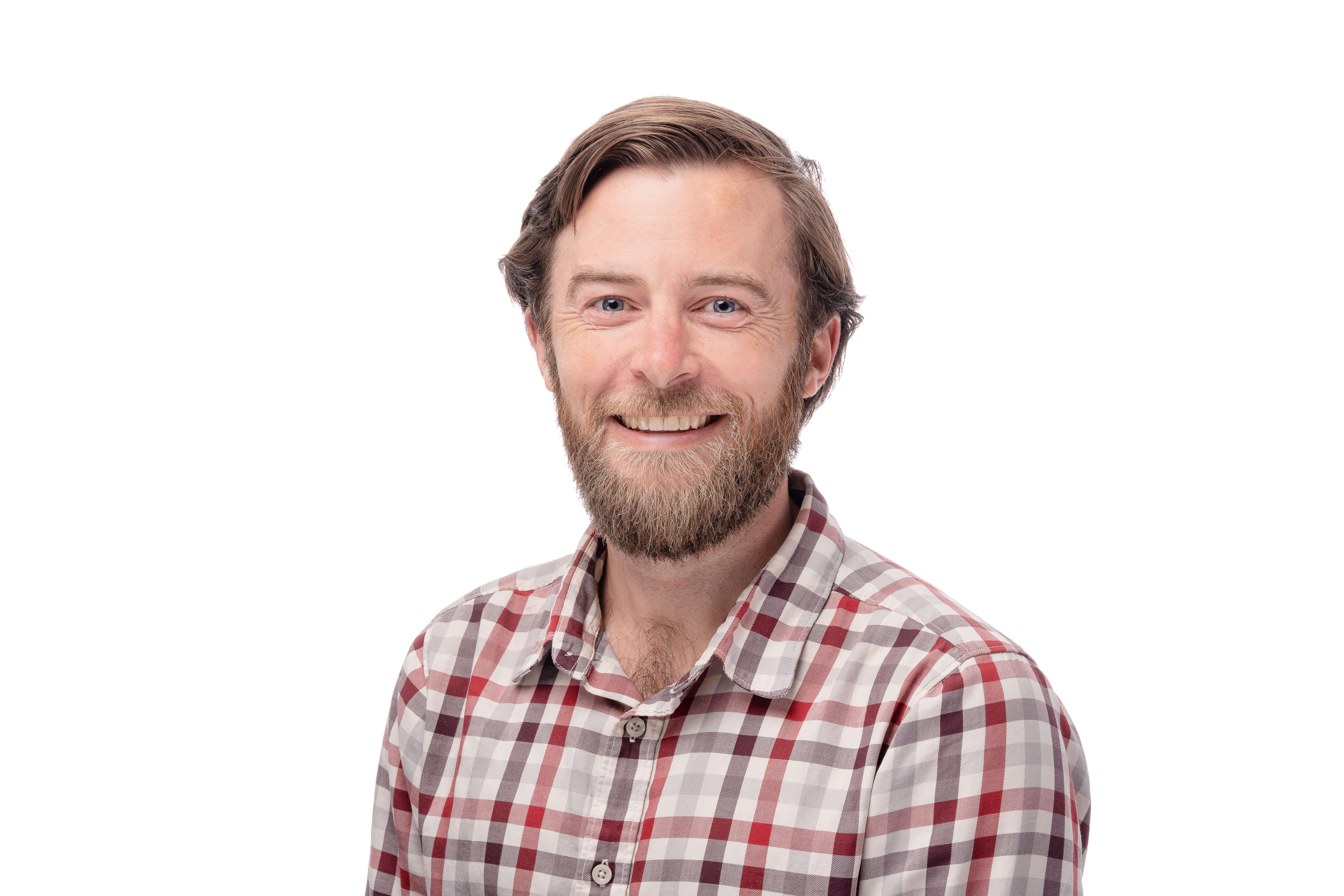 A headshot of a man with a beard and a warm smile, wearing a checked shirt. His casual, approachable demeanor is enhanced by the crisp white background.