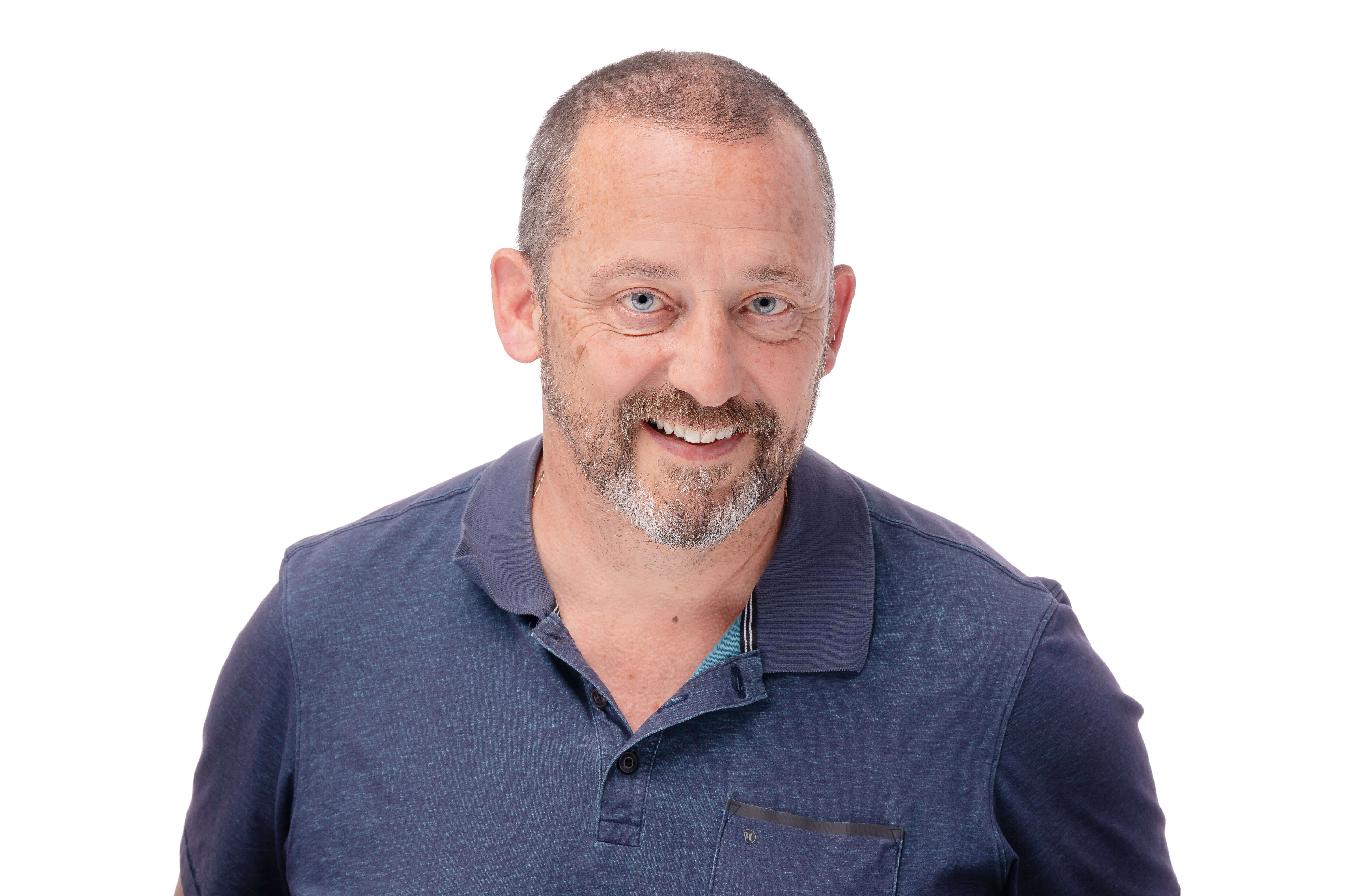 A headshot of a man with a closely cropped beard and a warm, engaging smile. He's wearing a casual navy polo shirt and the white background ensures his friendly expression is the focus of the image.