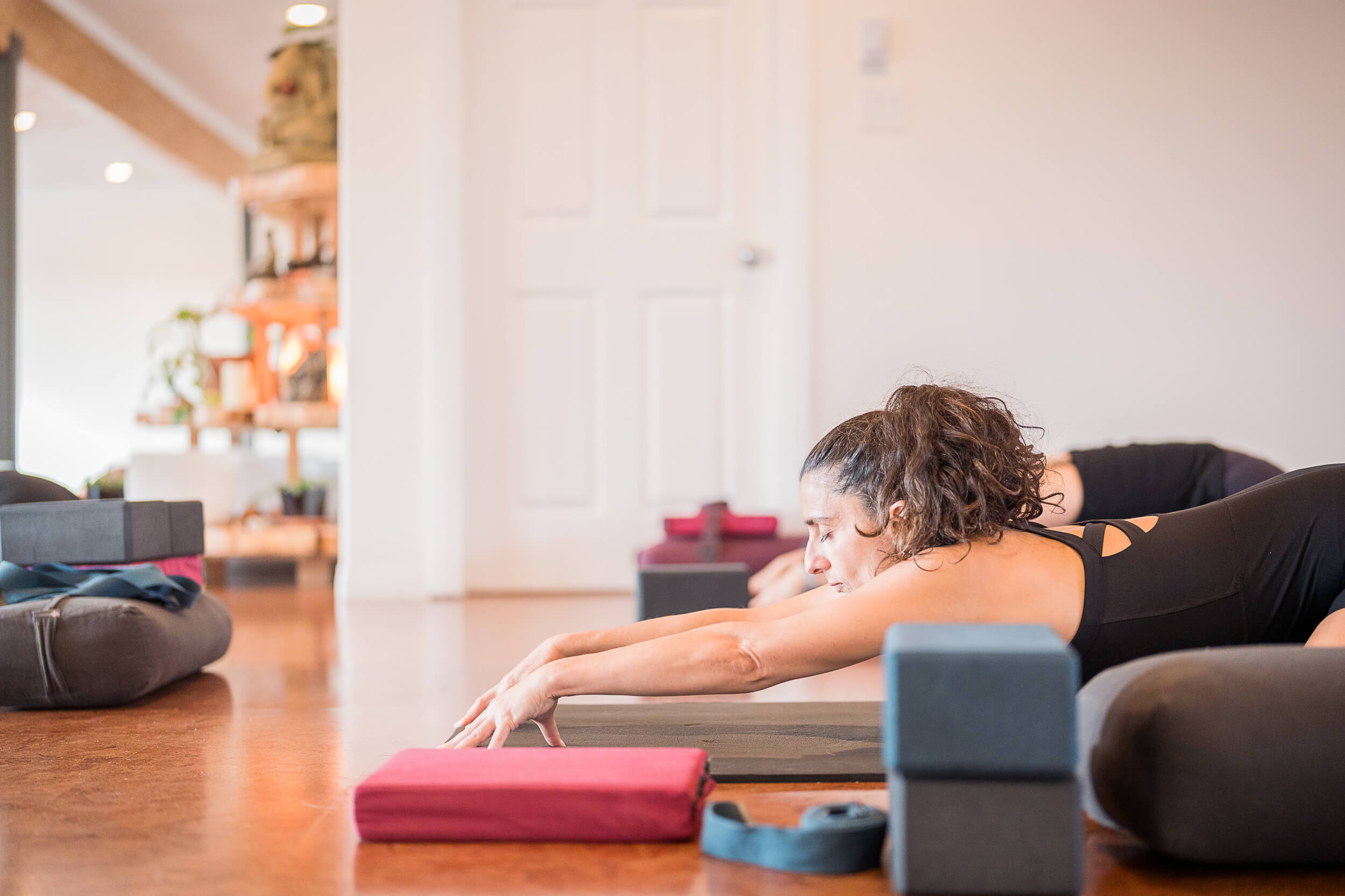 A focused yogi engages in a forward stretch at Shala Yoga in Squamish, demonstrating the quiet dedication that the studio nurtures in its tranquil environment, complete with warm wooden floors and a backdrop of yoga props that assist in the practice.