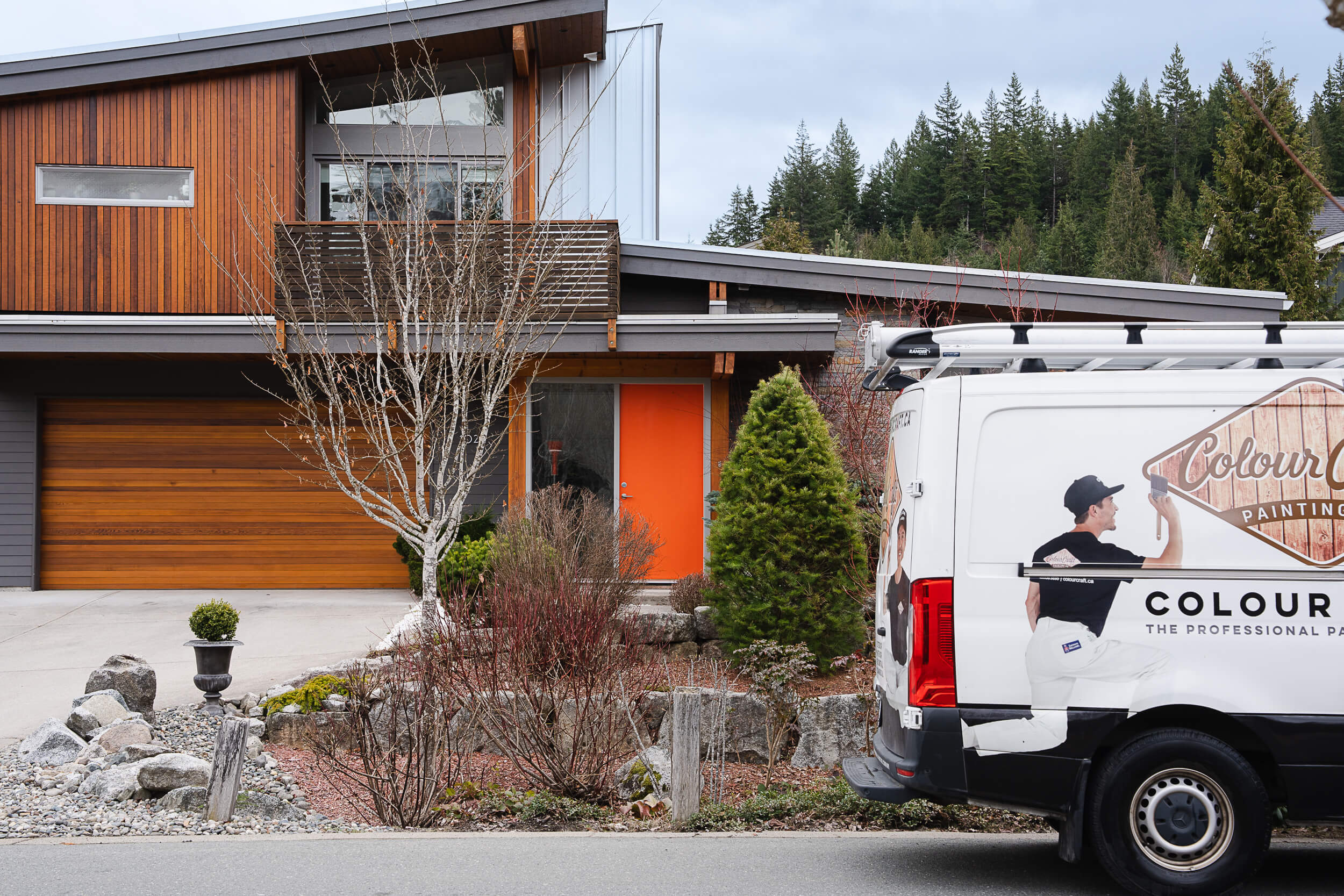 Captured in this lifestyle photography scene is the Colour Craft Painting van parked outside a modern home with striking wood and orange accents. The image reflects the company's active presence in the community, poised to deliver quality painting services.