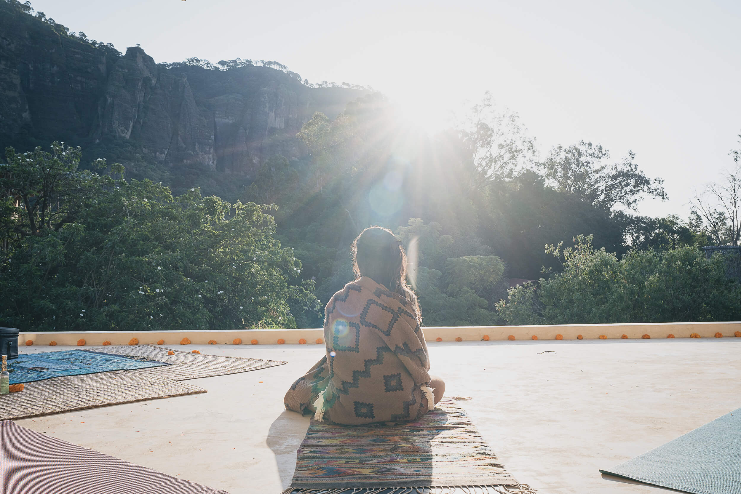 A serene morning yoga session in nature, with a participant meditating facing the sun, surrounded by majestic cliffs and lush greenery, in a photo by Matt Anthony Photography emphasizing lifestyle photography.