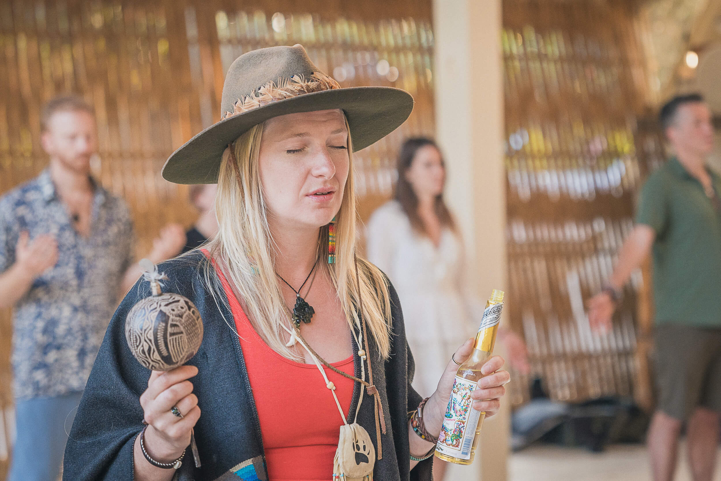 Lifestyle photographer captures a spiritual ceremony with a focused woman in a hat holding a maraca and a bottle of Agua de Florida, with participants in meditation in the background.