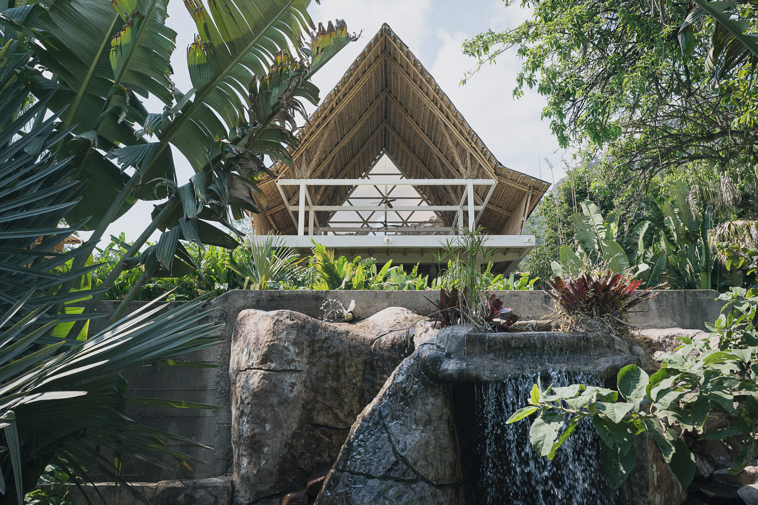 Scenic view of a luxurious, eco-conscious Mexican retreat captured by Matt Anthony Photography, featuring a traditional thatched roof pavilion amid rich tropical foliage with a serene waterfall, exemplifying top-tier lifestyle photography.