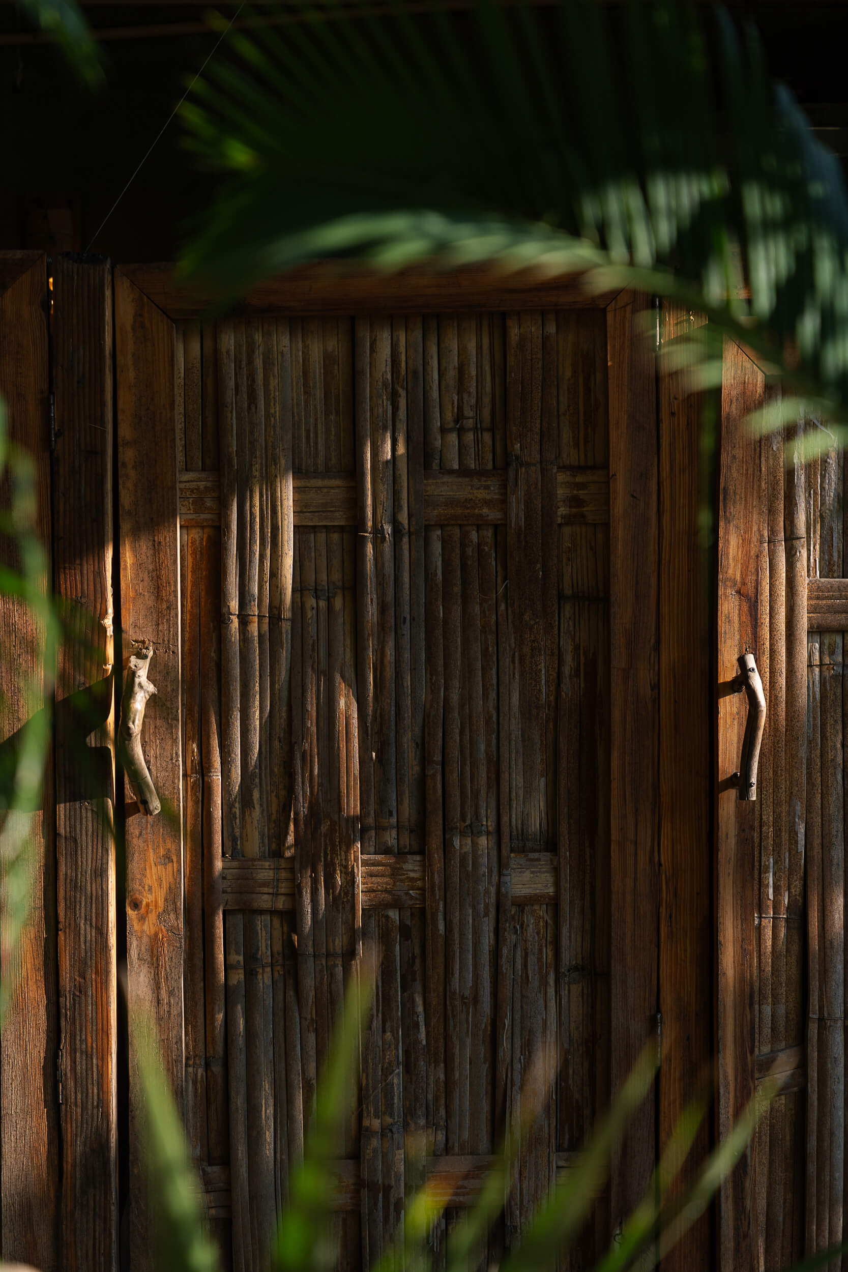 Rustic bamboo and wood doorway framed by lush tropical leaves at Amate Retreat Centre