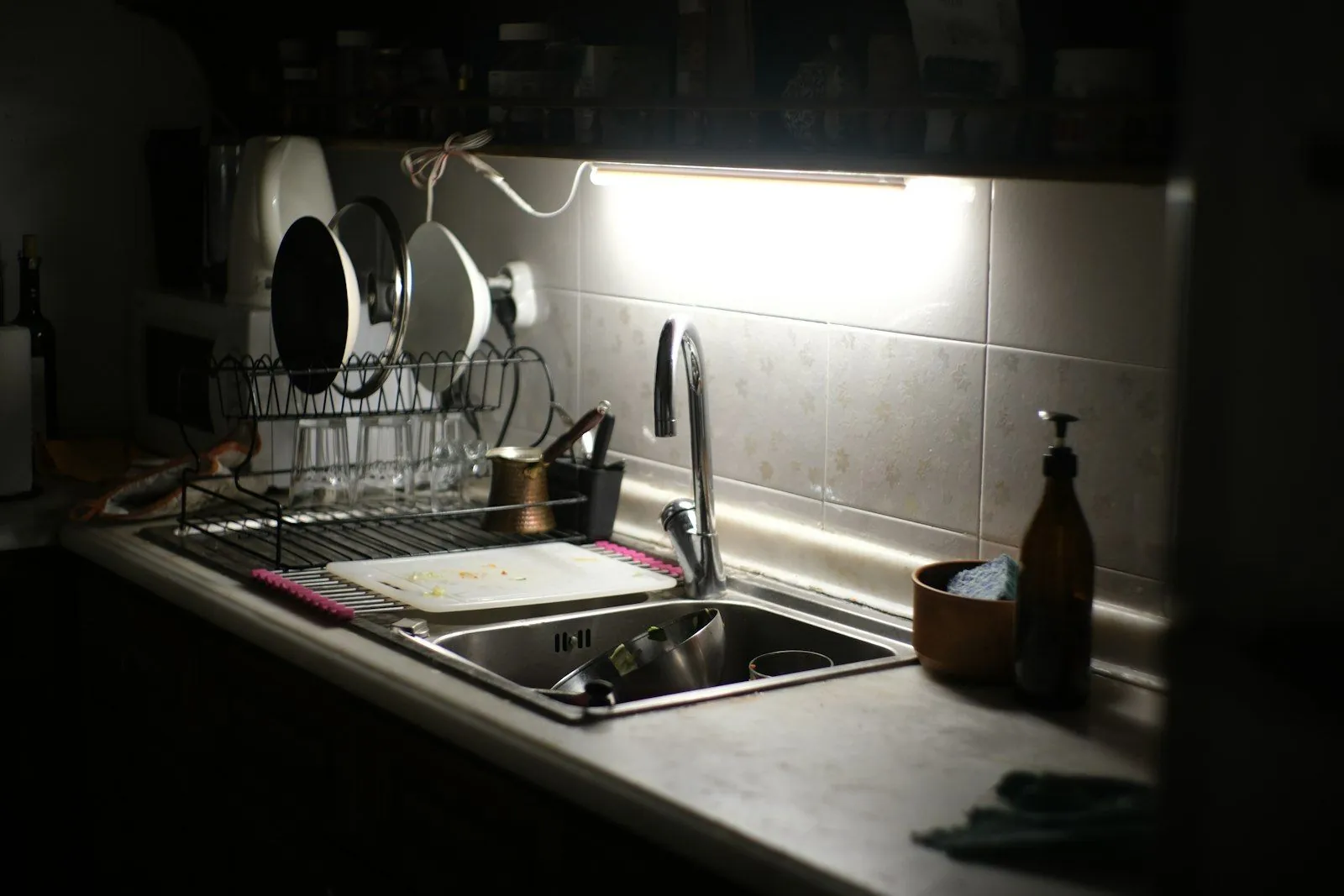 A kitchen sink lit by an under-cabinet light late at night