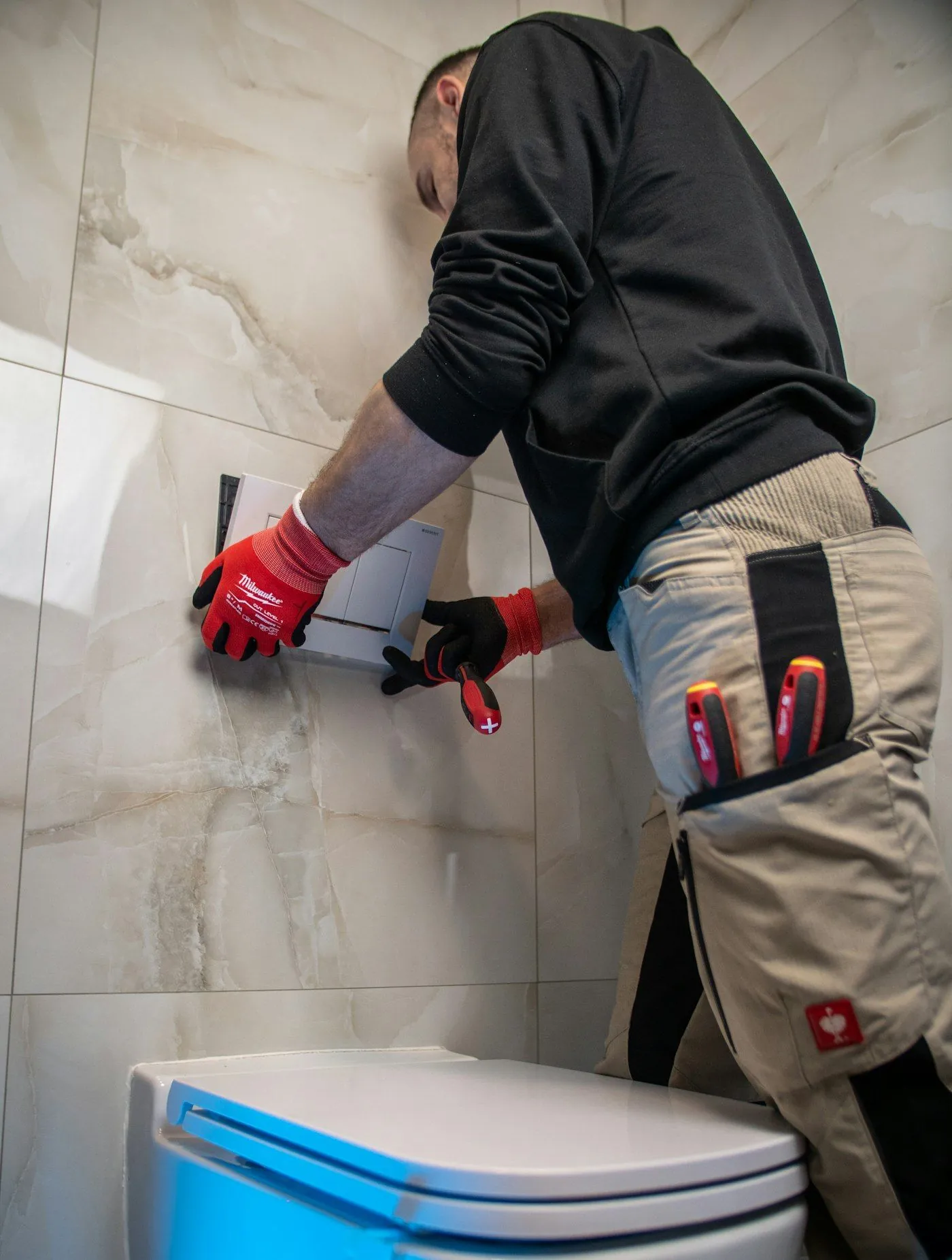 A technician working on a wall-mounted toilet in a tiled bathroom