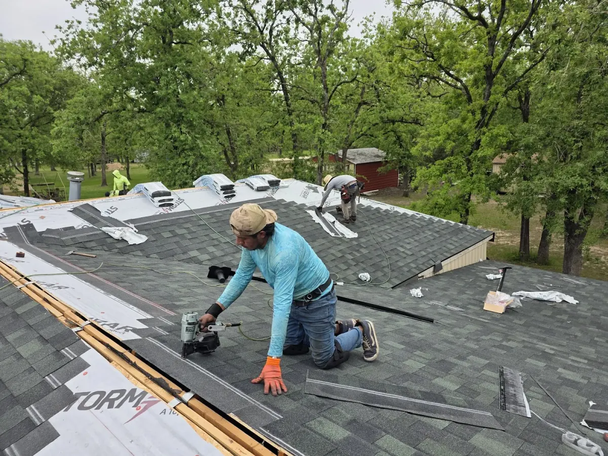 Roofer kneeling on a roof nailing down new gray architectural shingles