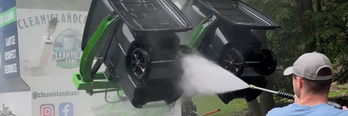 Worker pressure washing trash bins using professional cleaning truck system.