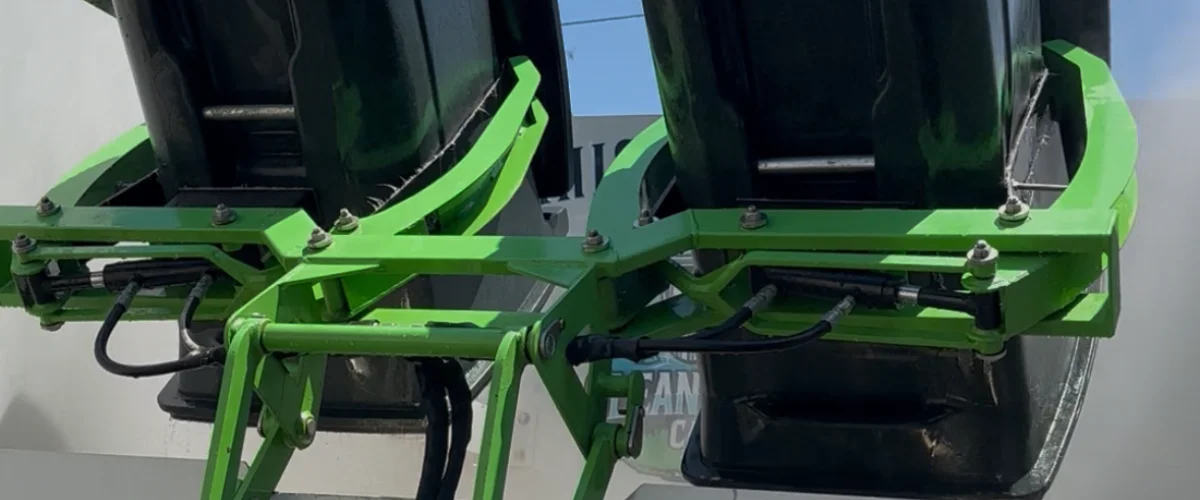 Close-up of a lime green hydraulic lifting mechanism for two black refuse bins on a sunny day.